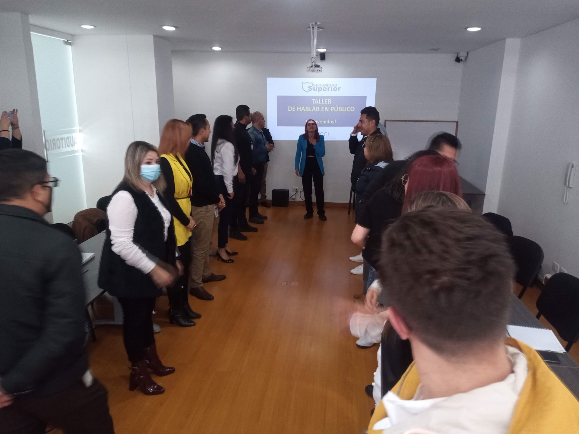 Personas en una presentación. Una mujer frente a una pantalla de proyección se dirige al público en una sala.