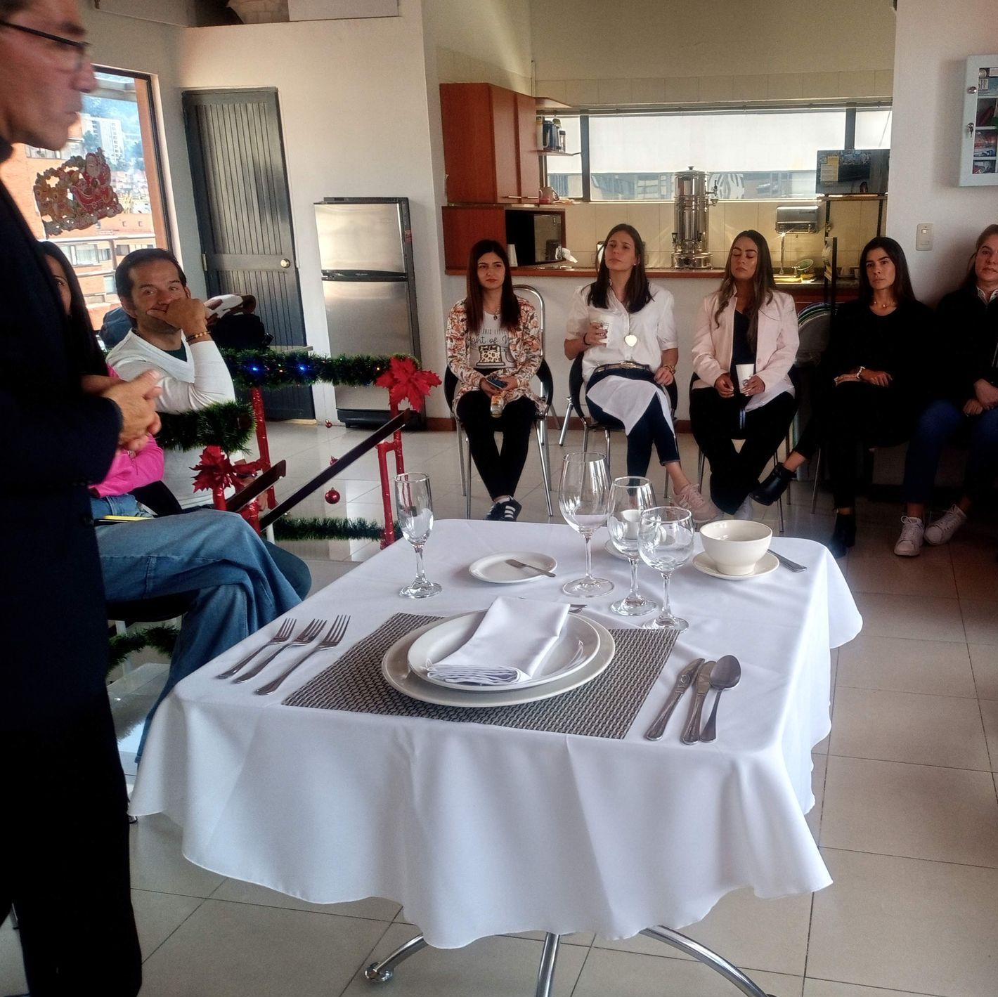 Personas sentadas alrededor de una mesa mientras alguien habla. Mesa formal.