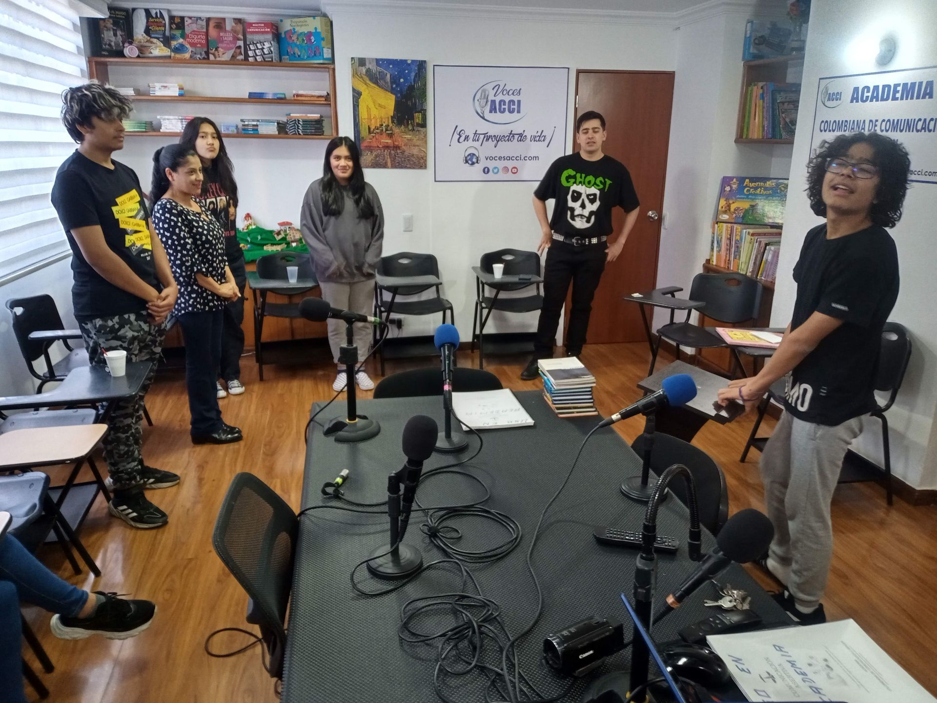 Grupo de personas en un estudio de grabación alrededor de una mesa con micrófonos. Algunos sonríen.