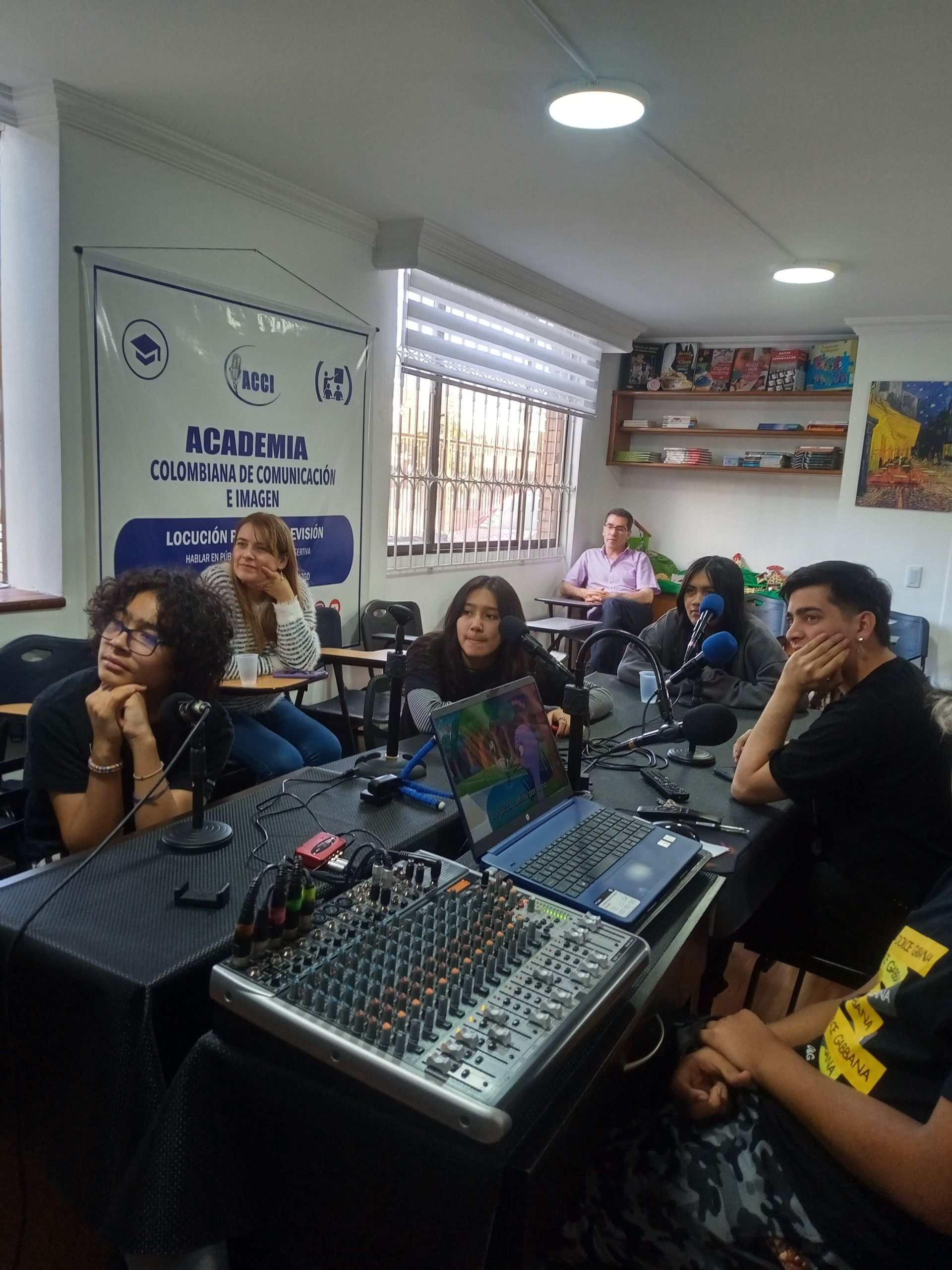 Personas en una mesa de estudio de grabación. Se ven micrófonos, equipo de mezcla de audio y material gráfico.