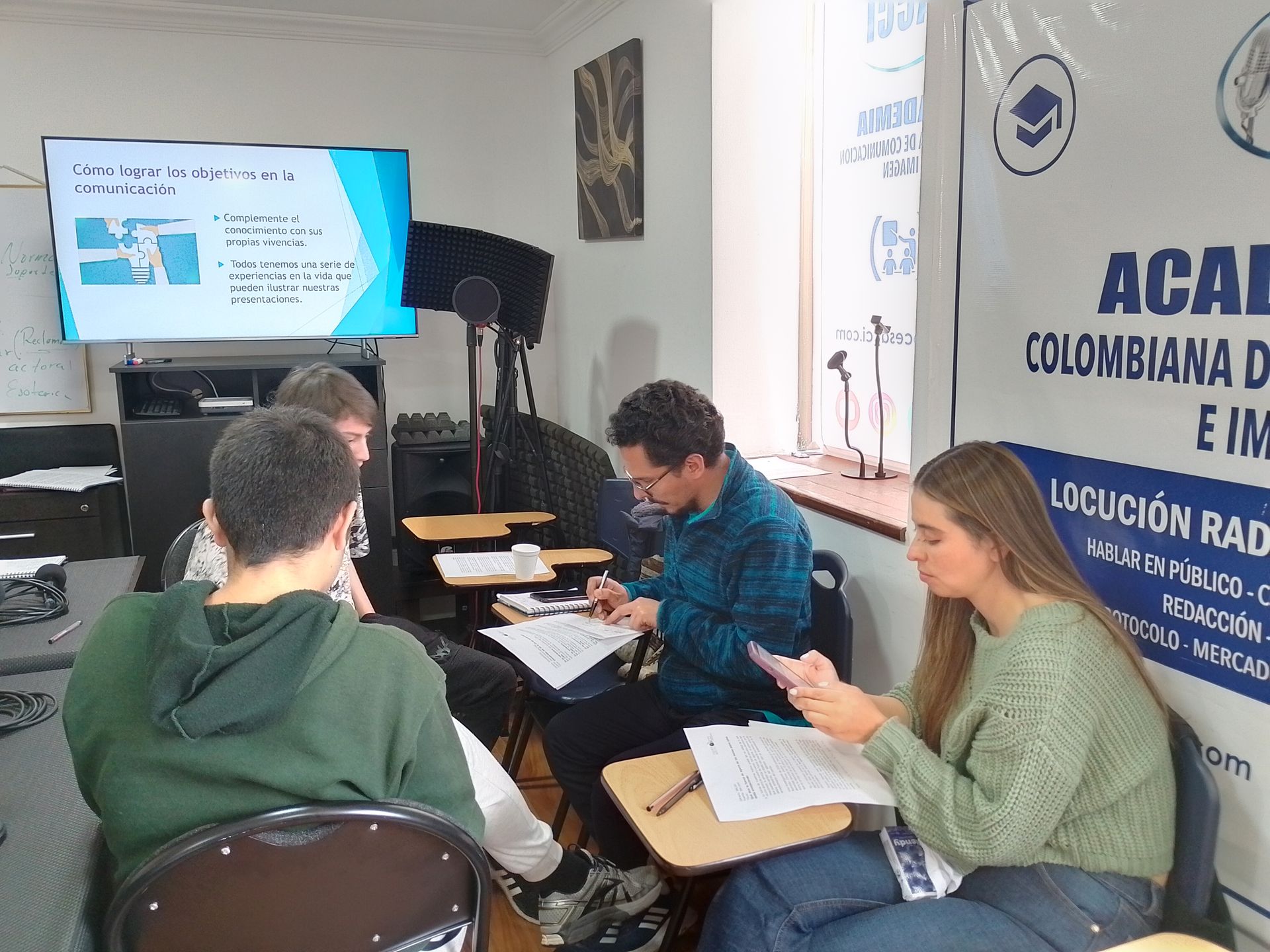 Cuatro personas en un aula; una presentación en pantalla. Los estudiantes están estudiando trabajos académicos.