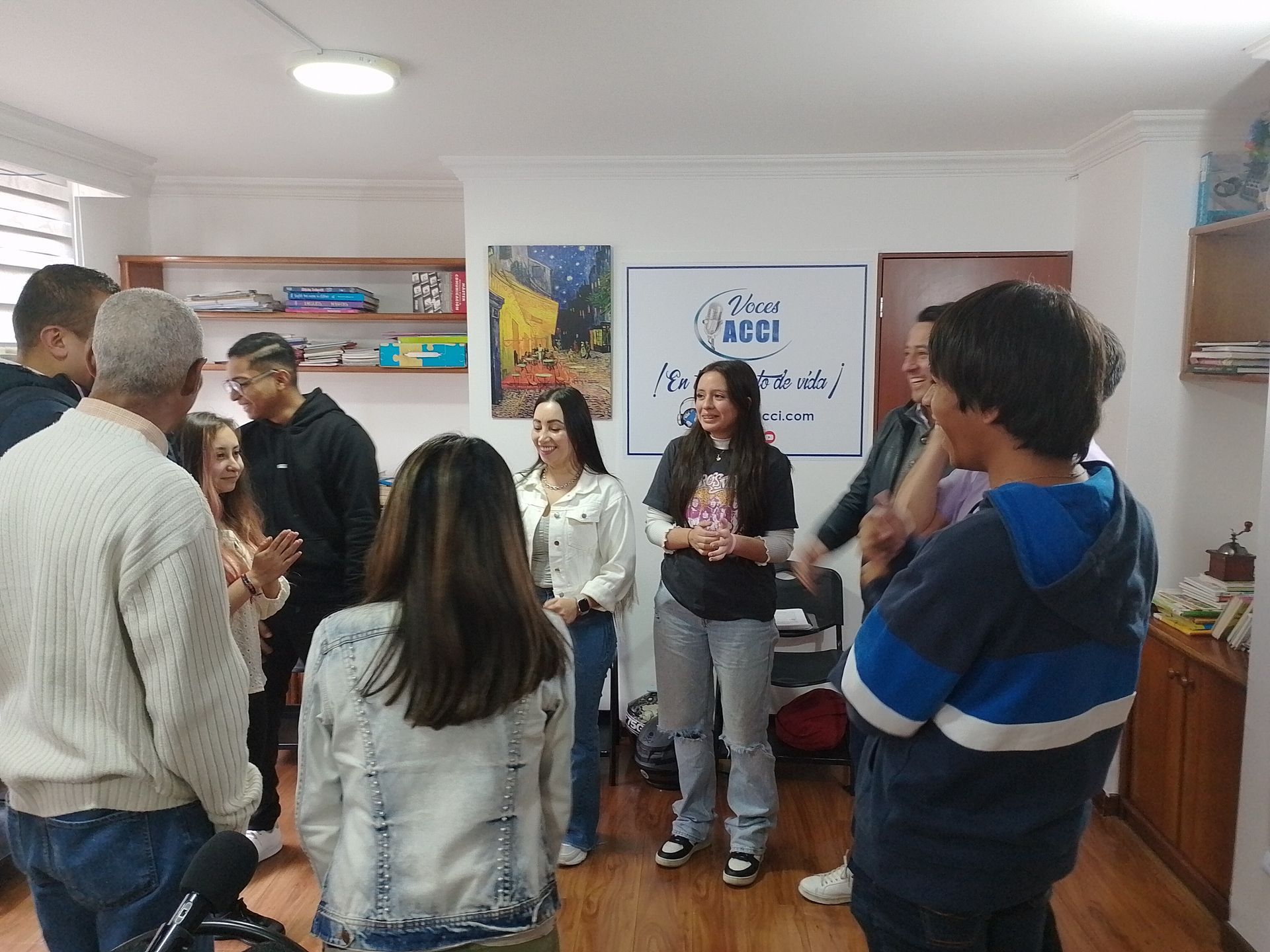 Grupo de personas en una habitación luminosa, algunas sonriendo. Se ve parcialmente un cartel en la pared.