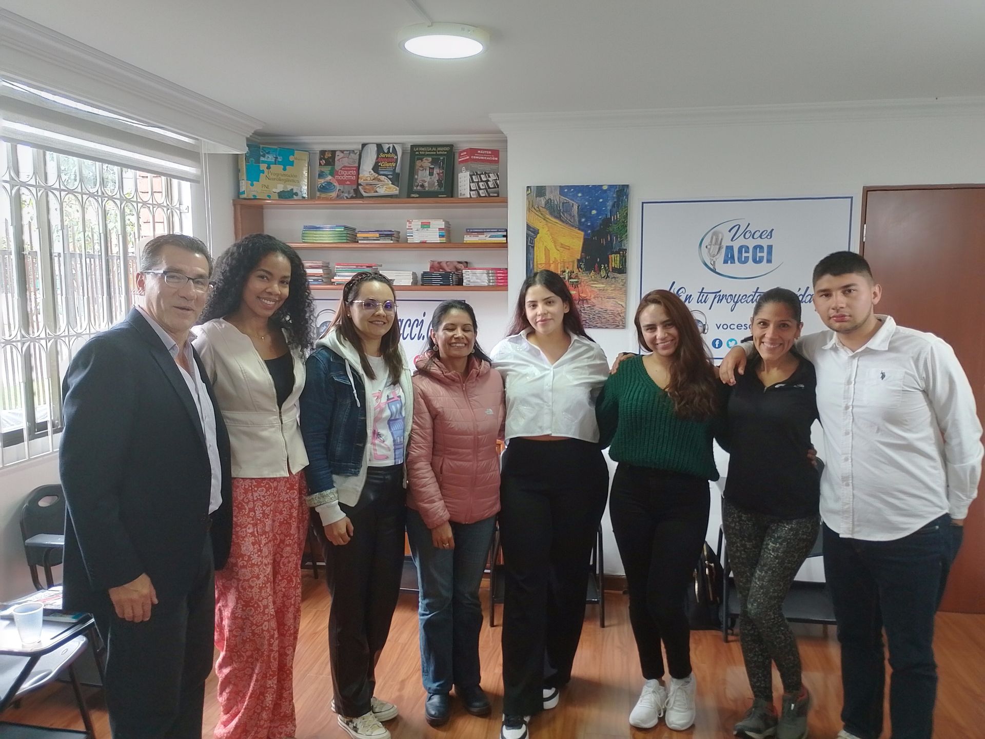Grupo de personas sonriendo, posando en una oficina, frente a un cartel.