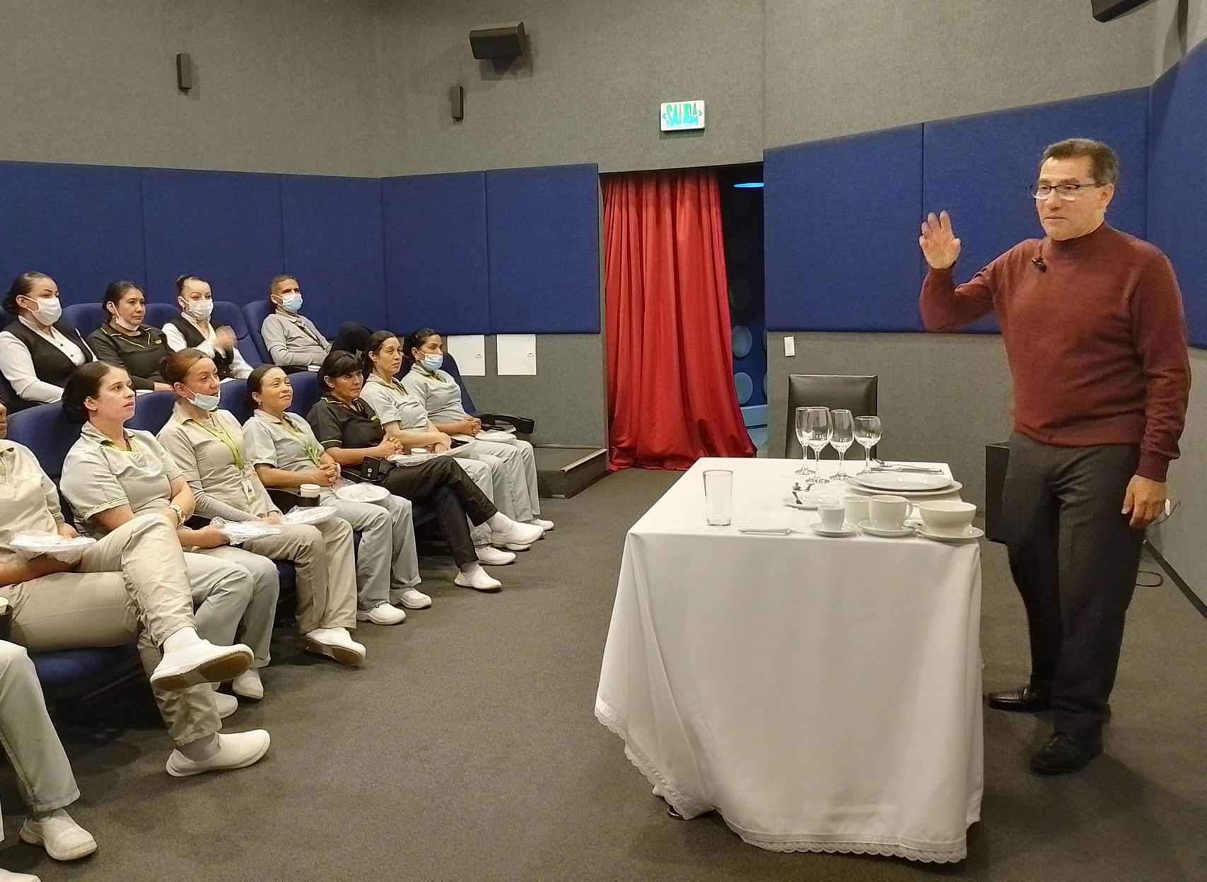 Hombre dando una presentación sobre la preparación de la mesa a un grupo sentado.