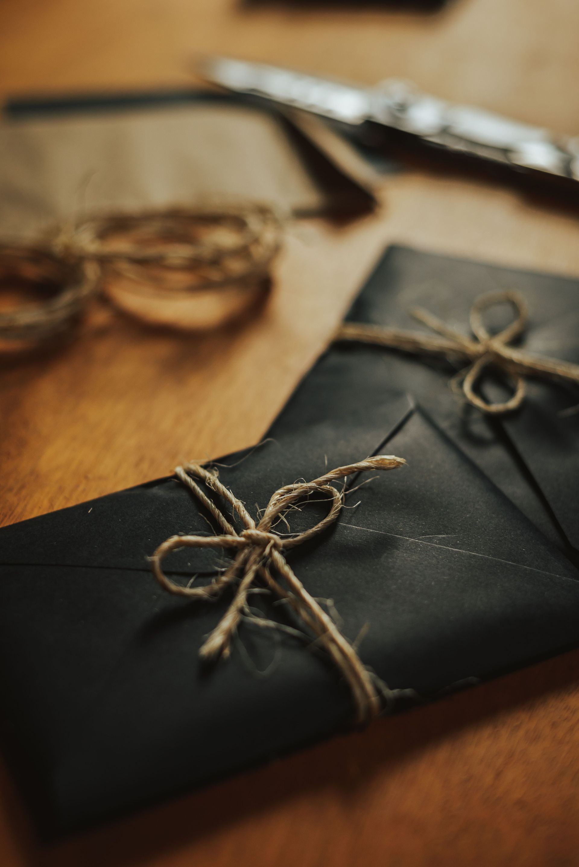 Gift-wrapped black envelope tied with twine on a wooden table, with blurred kraft string and scissors nearby
