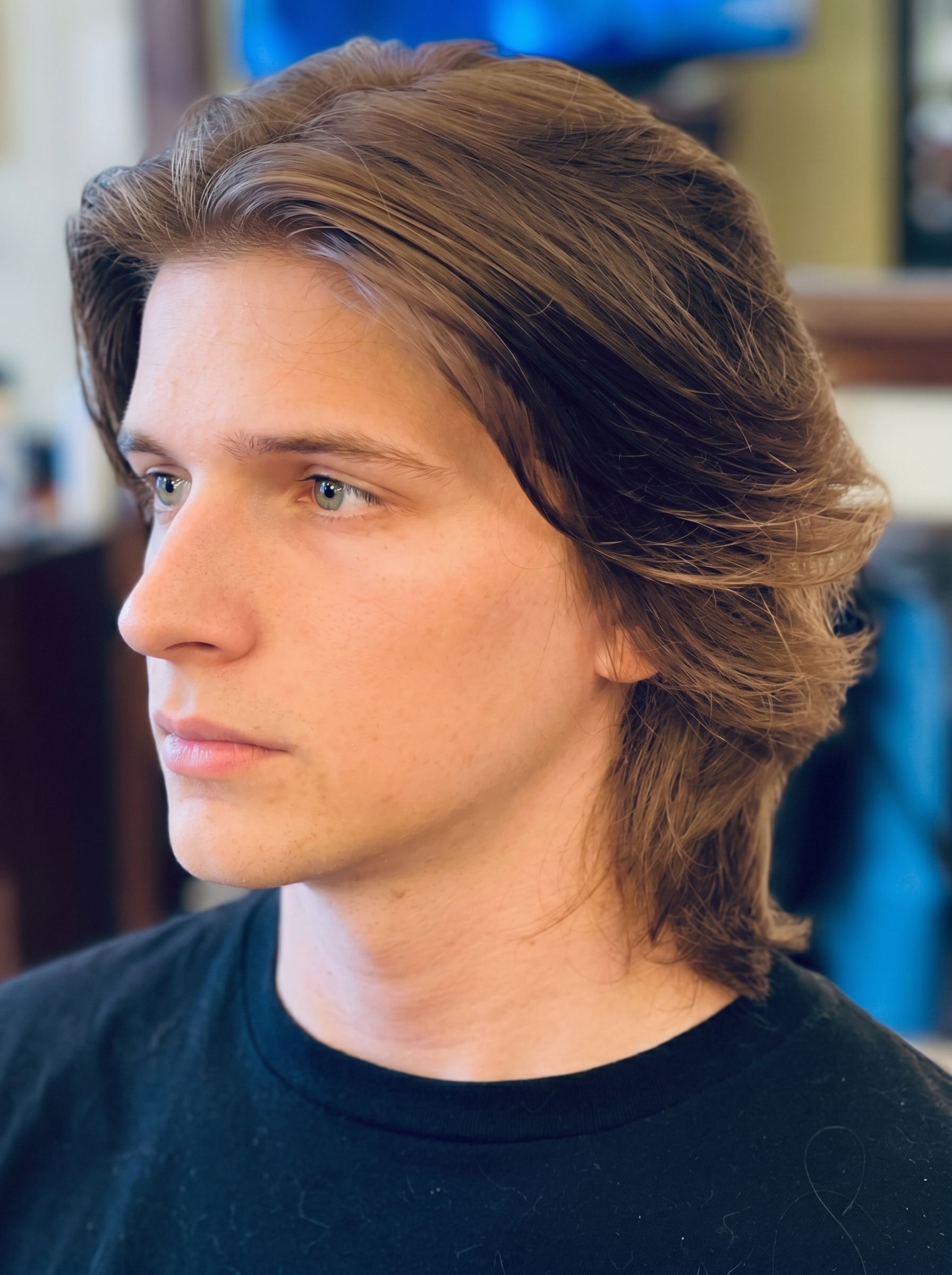 Profile view of a person with medium brown hair wearing a black shirt, looking left indoors
