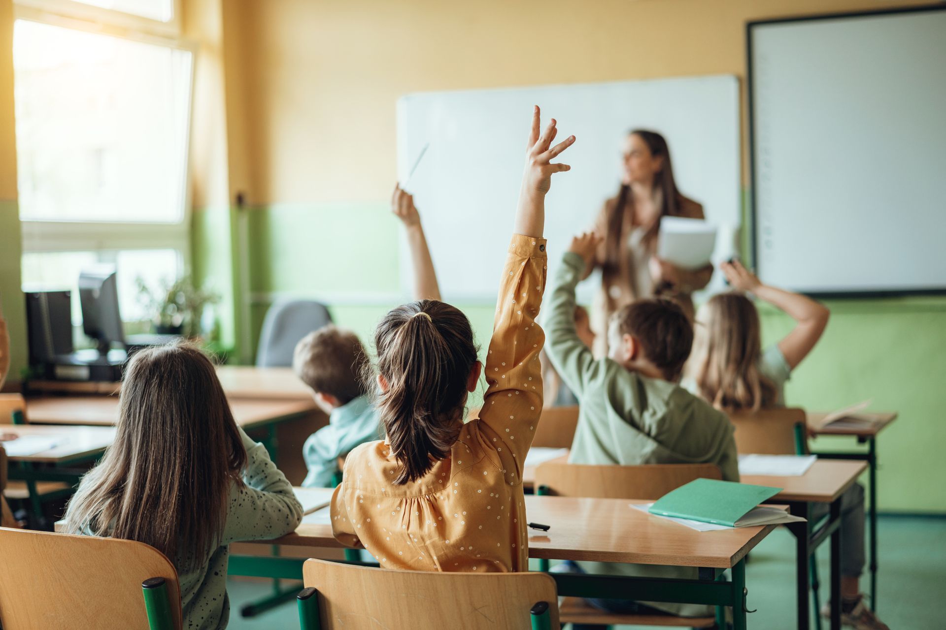 A group of children are raising their hands in a classroom to answer a question.