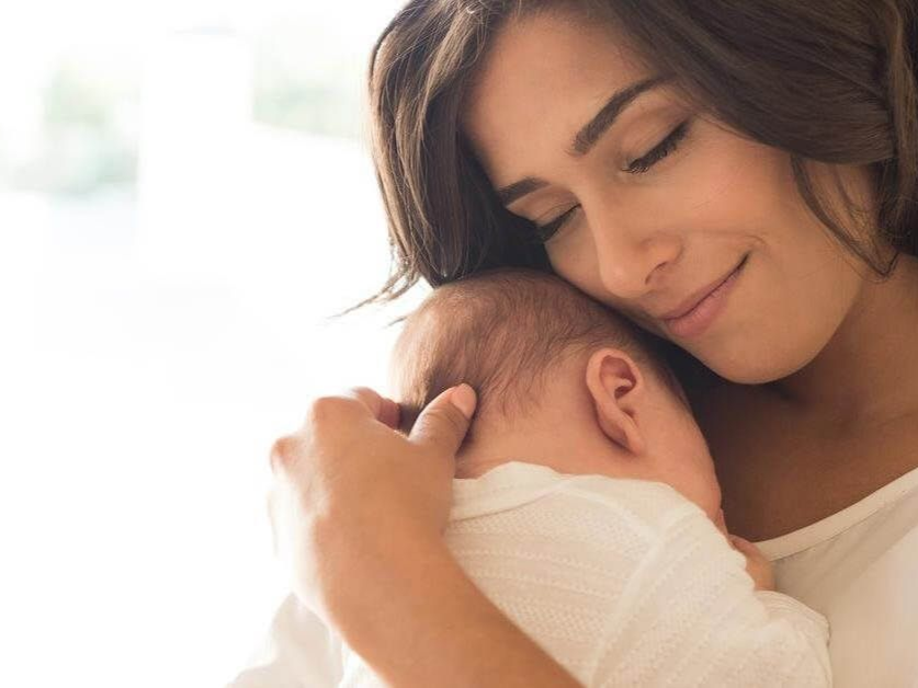 Woman gently holding a sleeping baby against her shoulder in a soft, bright setting