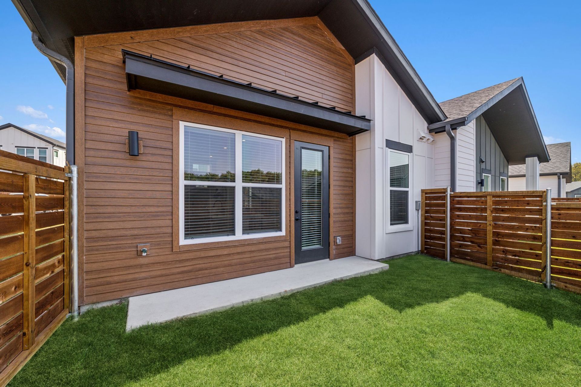 Modern brick house exterior with front lawn, wooden fence, and large windows