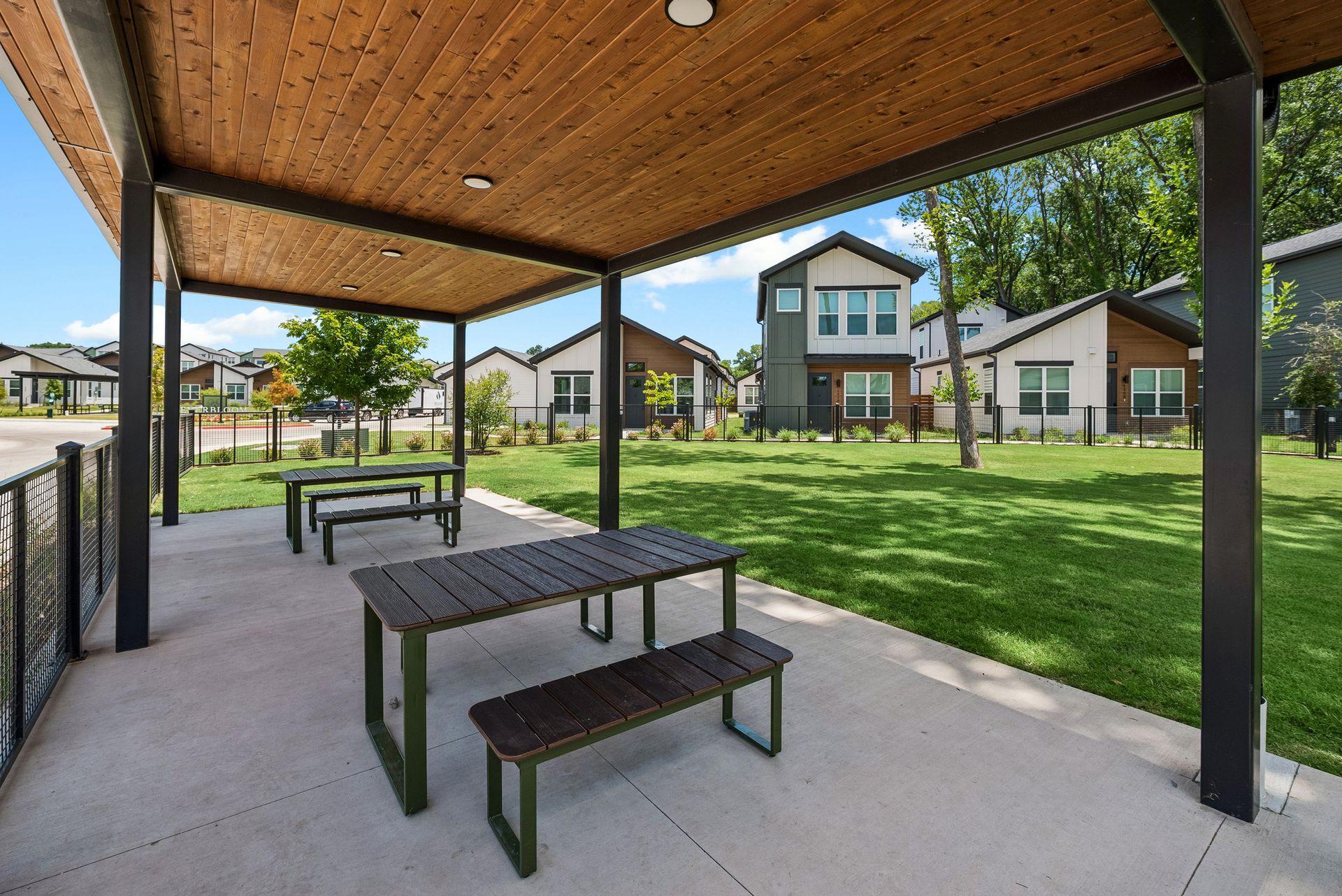 Covered picnic area with tables overlooking a grassy apartment courtyard with townhomes and trees