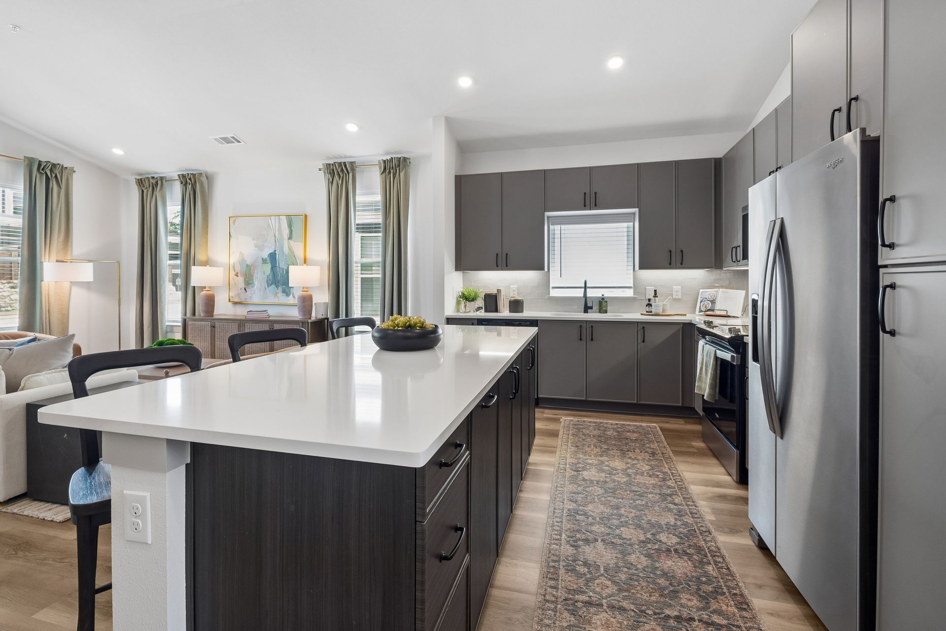 Modern kitchen with a large island, dark cabinets, stainless steel appliances, and a patterned runner rug.