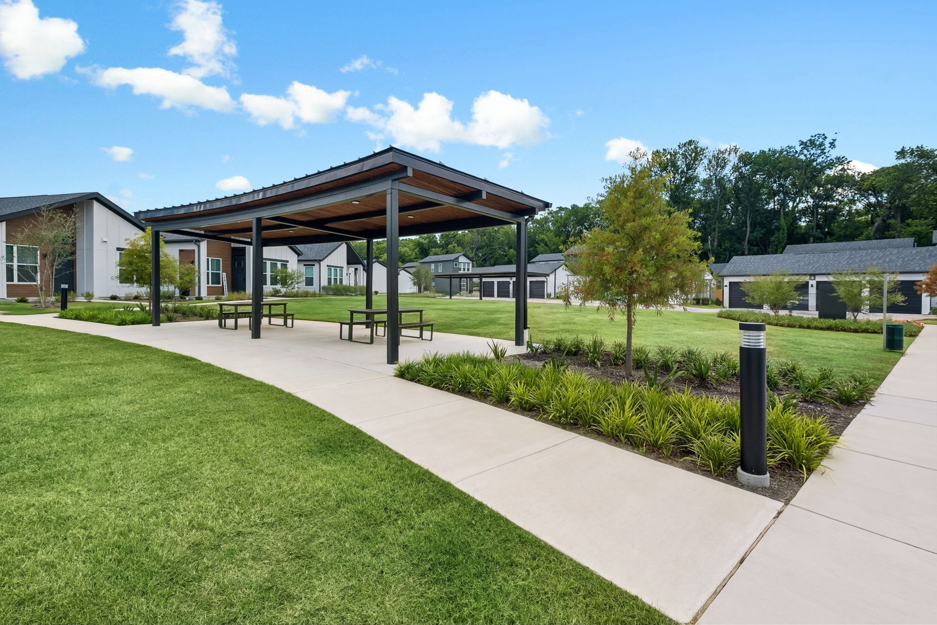Modern campus courtyard with covered walkway, green lawn, and paved paths under a blue sky
