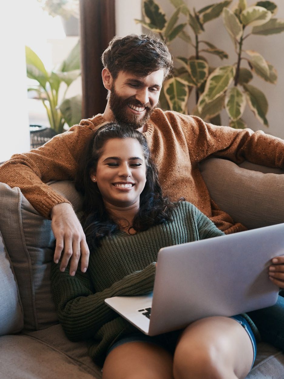 A man and a woman are sitting on a couch looking at a laptop.