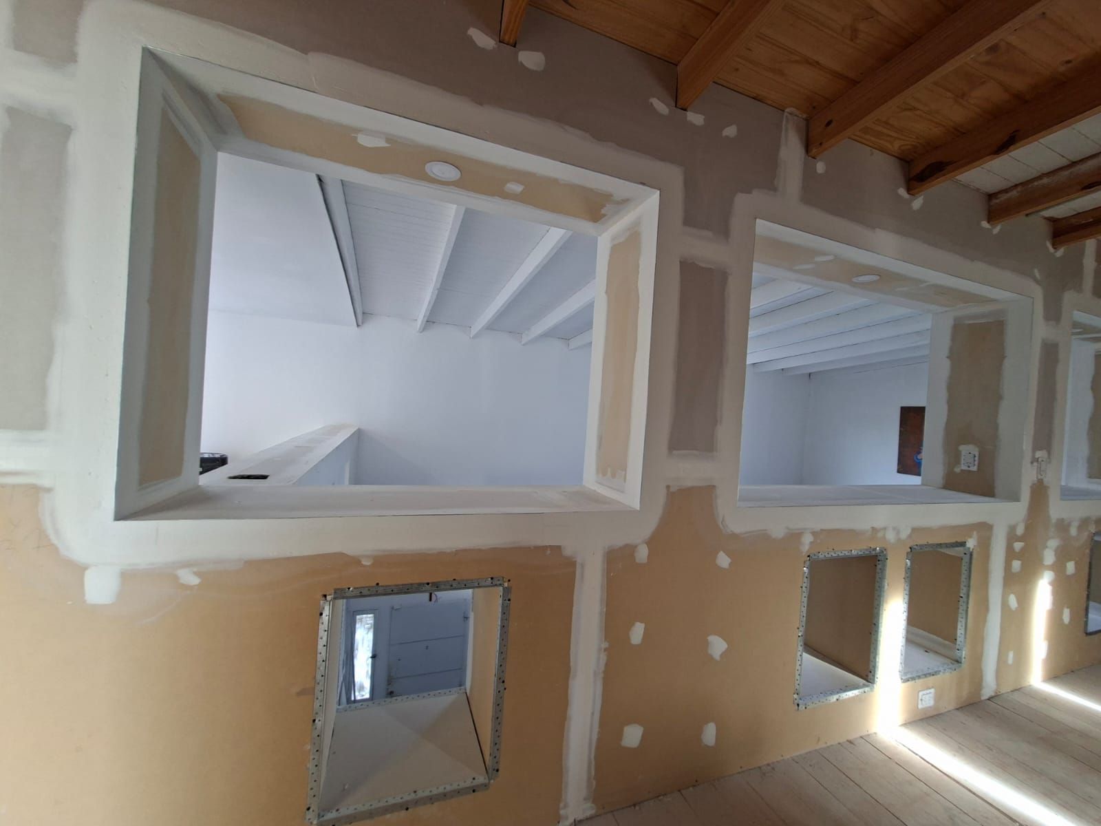 Construcción interior con paneles de yeso y marcos de ventanas; pared sin terminar con ventanas empotradas.