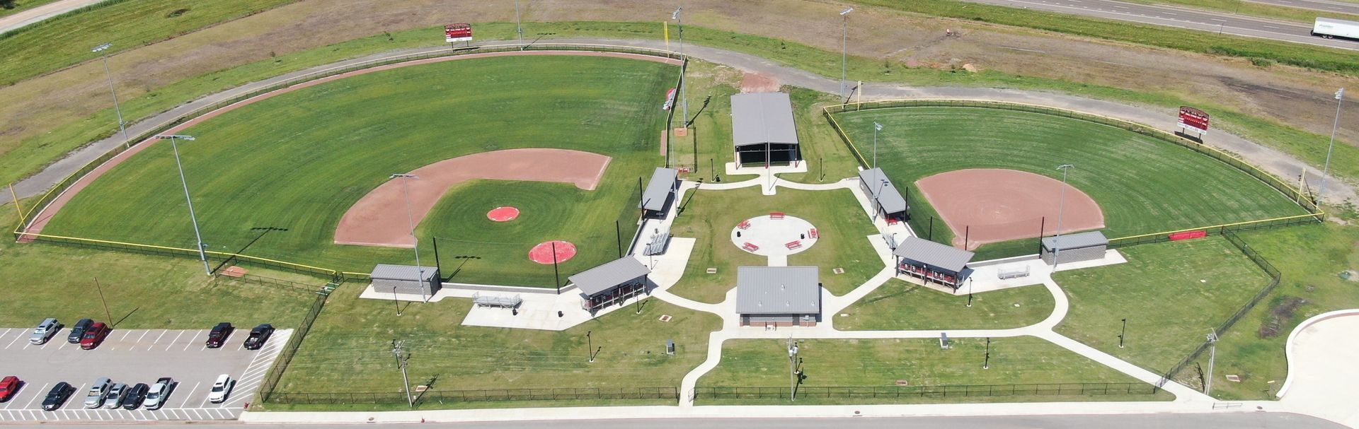 An aerial view of a baseball field with a parking lot in front of it