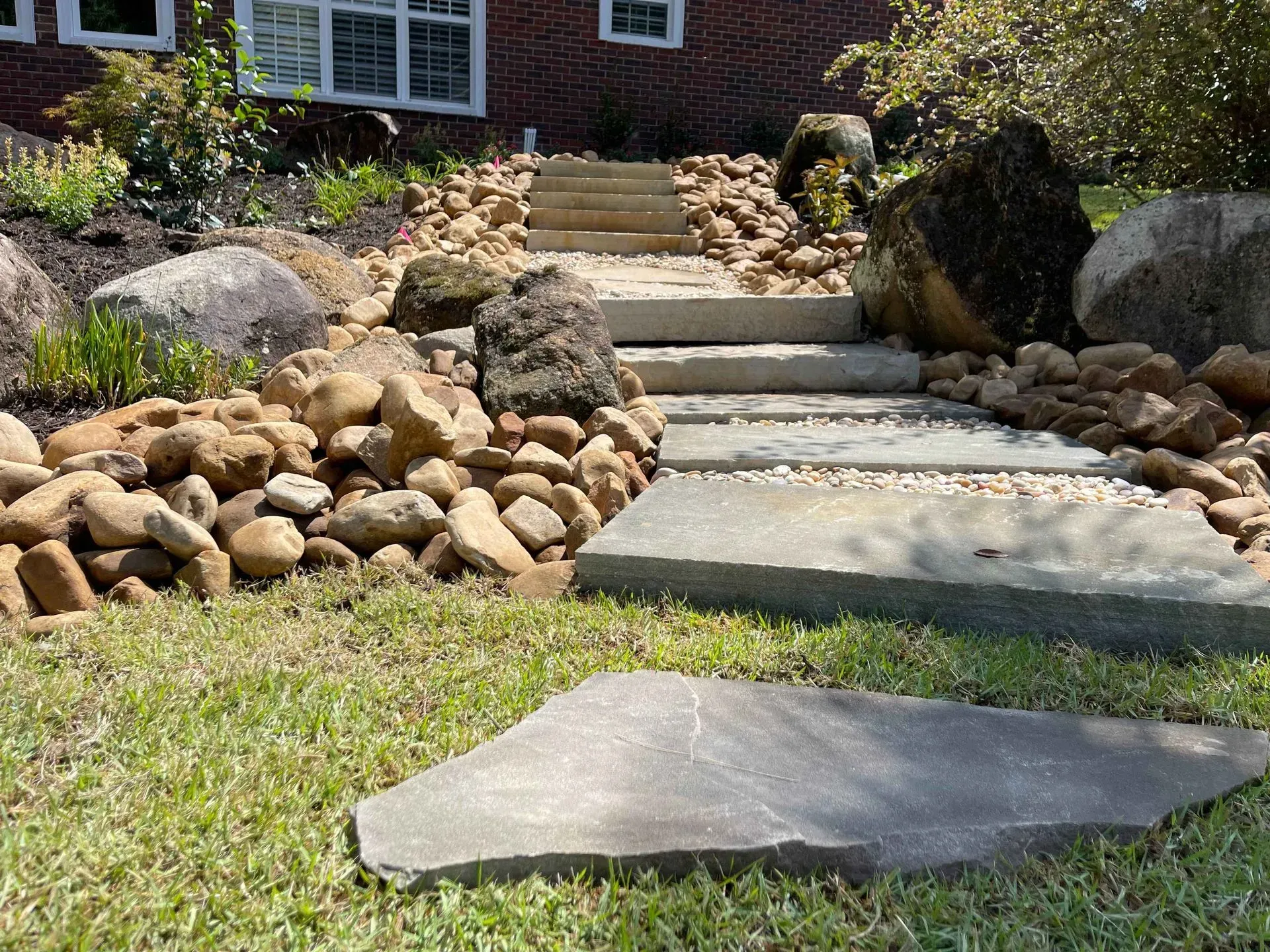 Stone steps and a front walkway leading up a landscaped yard to a brick house porch
