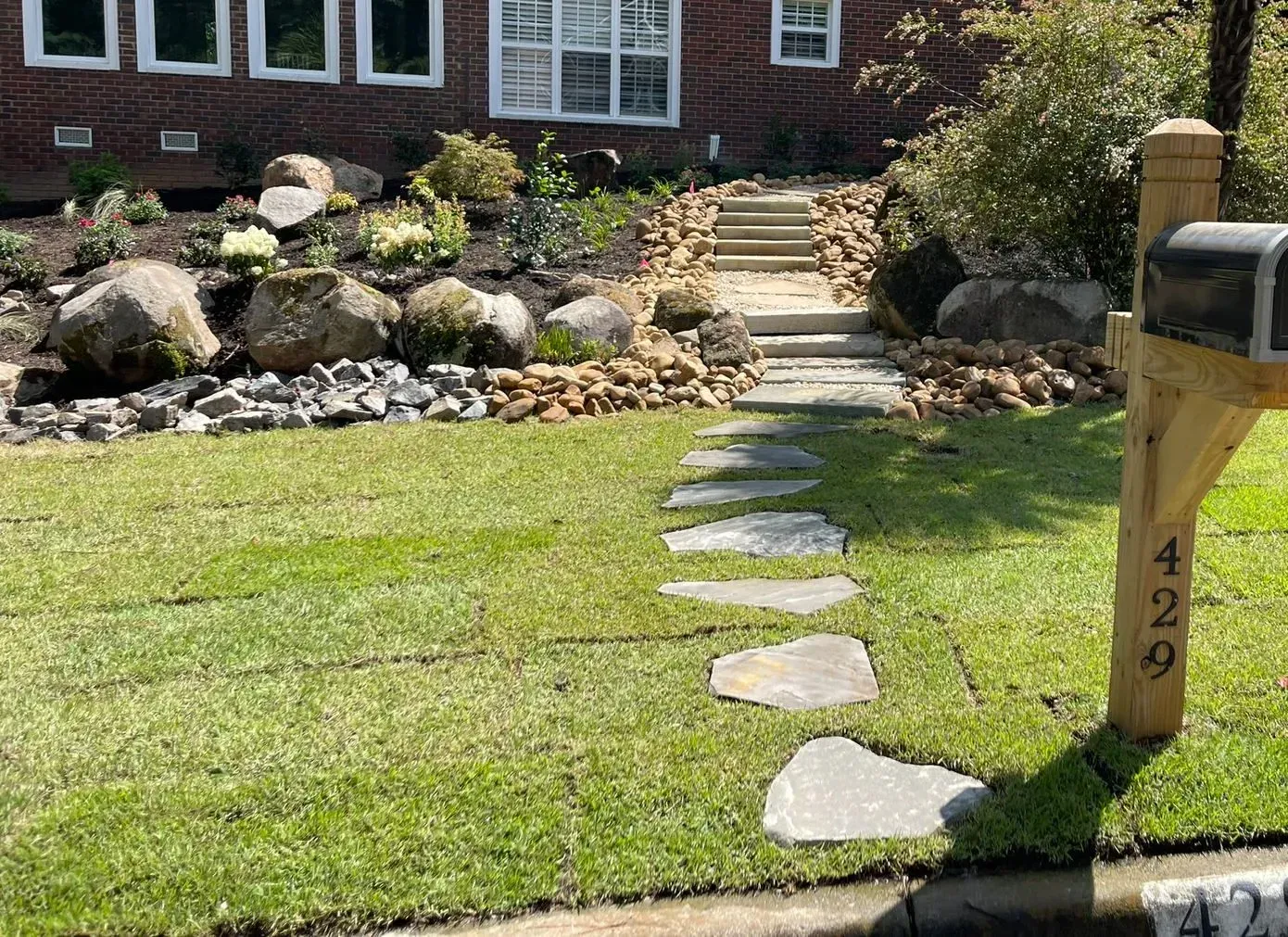 Front yard with stone path, green lawn, rock garden, and brick house steps.