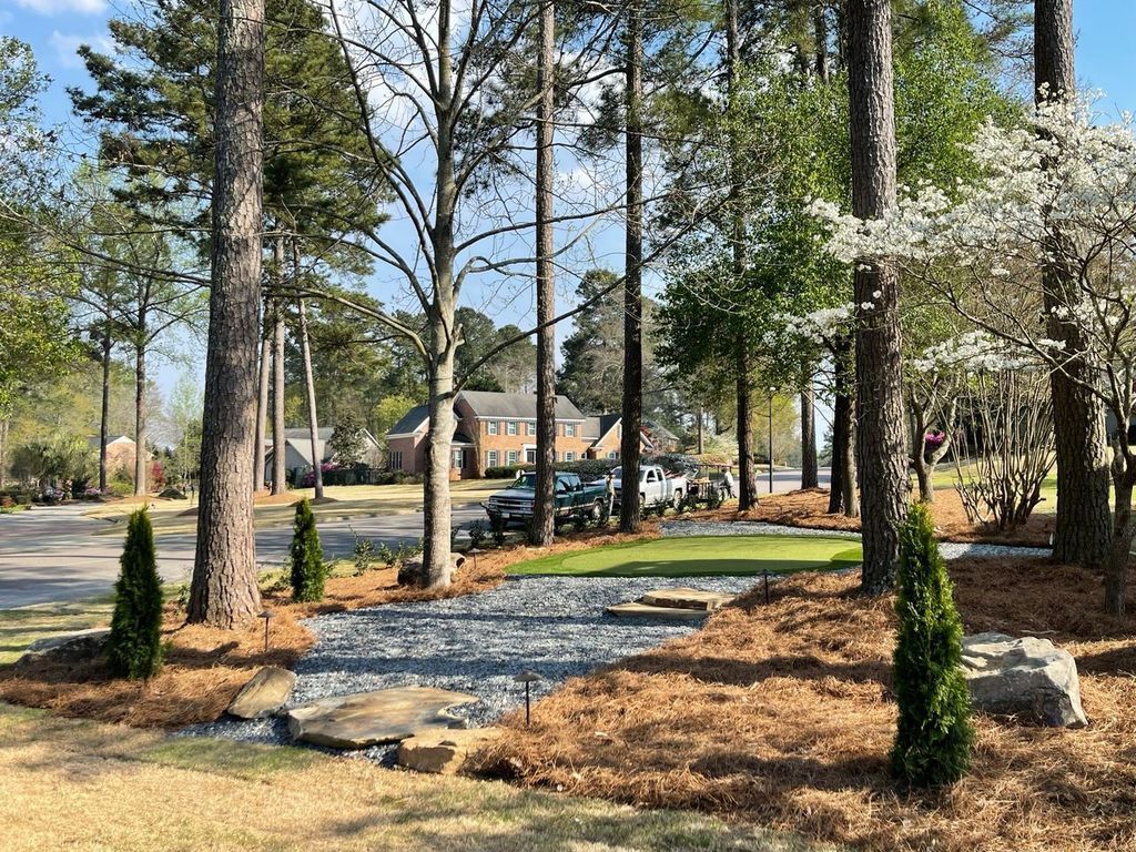 Landscaped yard with tall pine trees, gravel path, and a house in the background