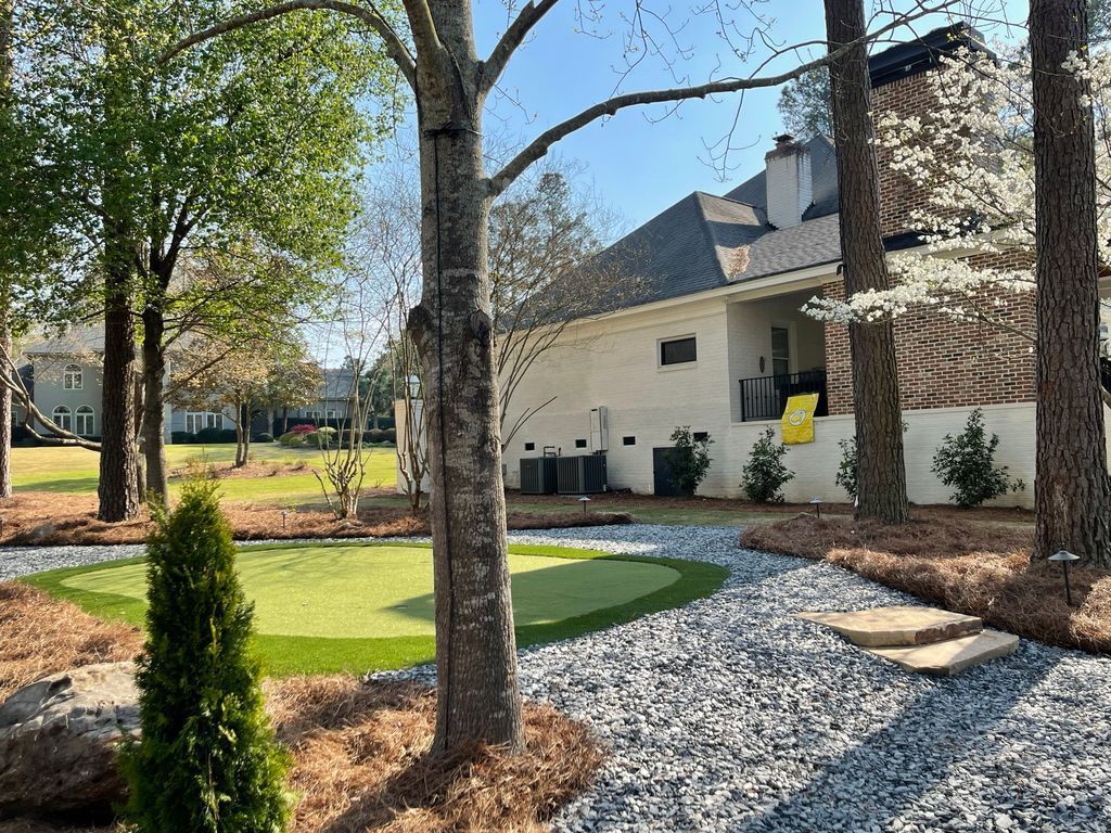 Leafy backyard with gravel path, trimmed lawn, trees, and a house under a blue sky