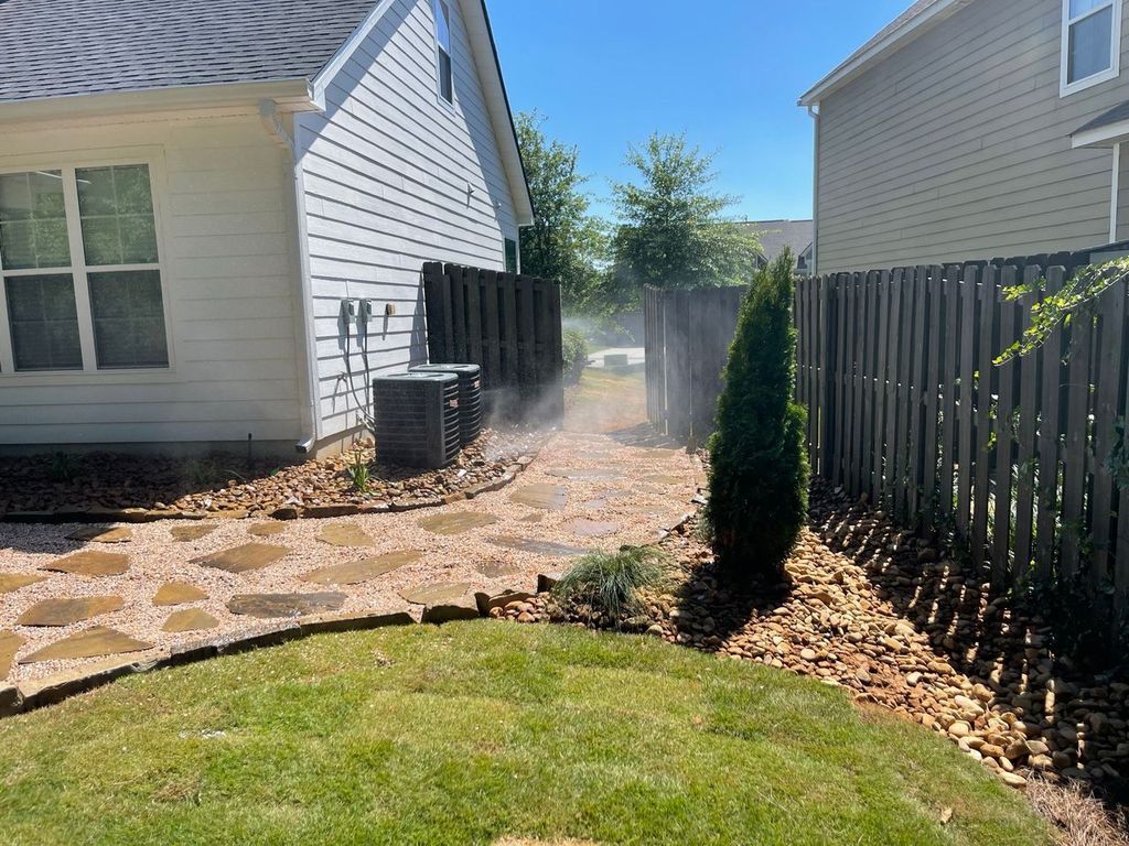 Backyard with stone path, green lawn, fence, and a small evergreen shrub near a house