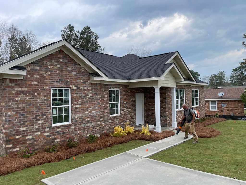 Brick house with white columns, a concrete walkway, and a person walking near the front porch