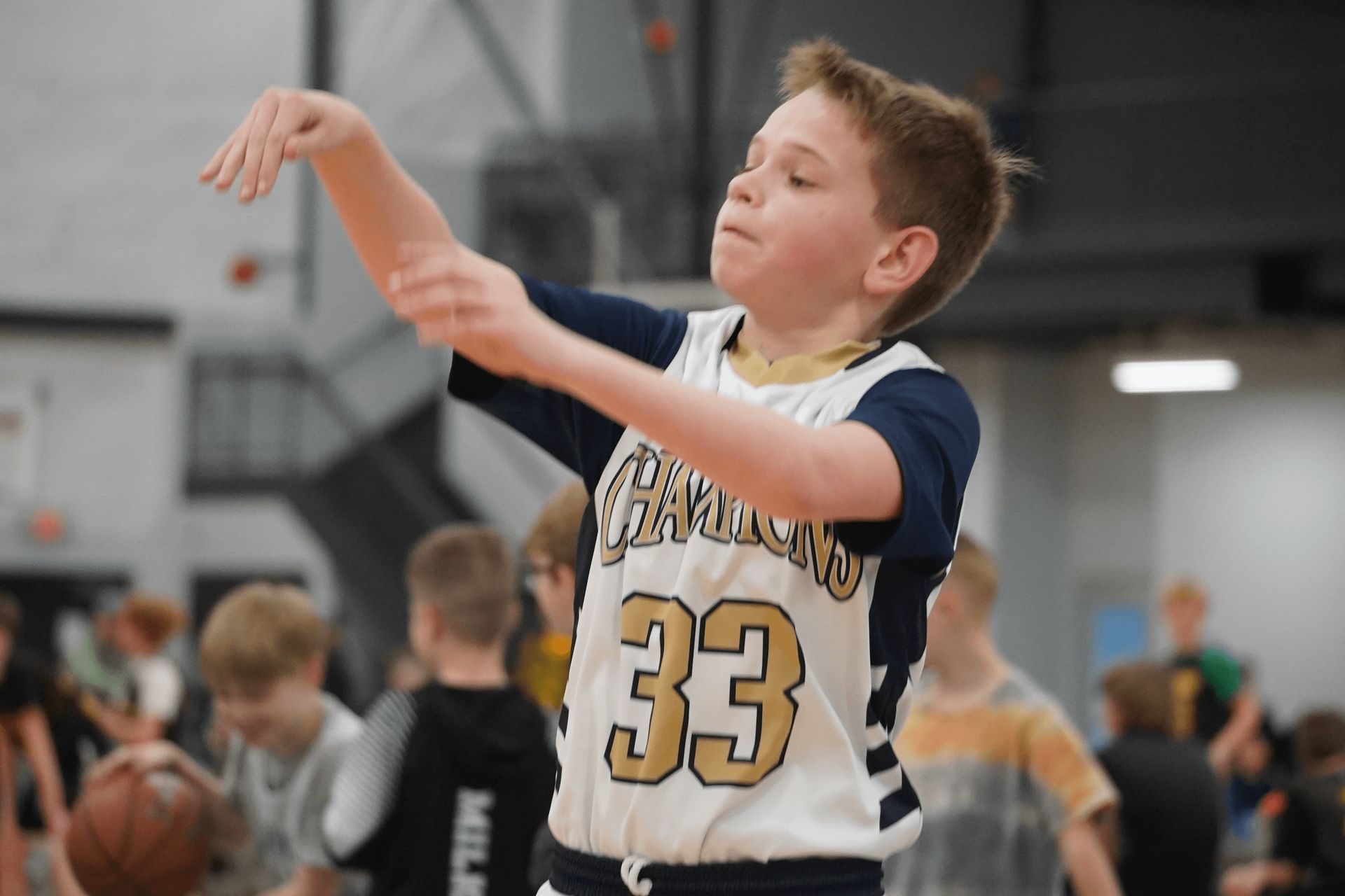 Young basketball player in a white jersey, number 33, practicing an arm movement on an indoor court
