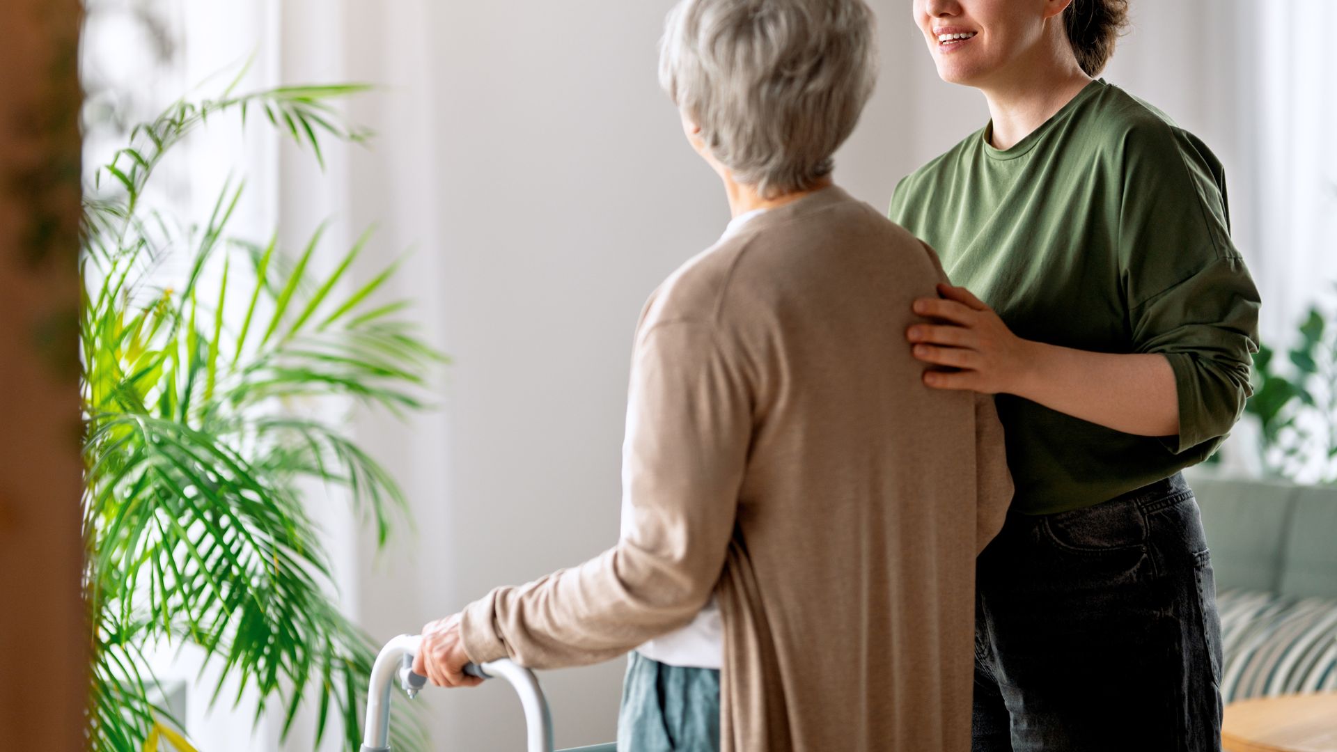 Caregiver assisting a person in a wheelchair with foot support in a bedroom.