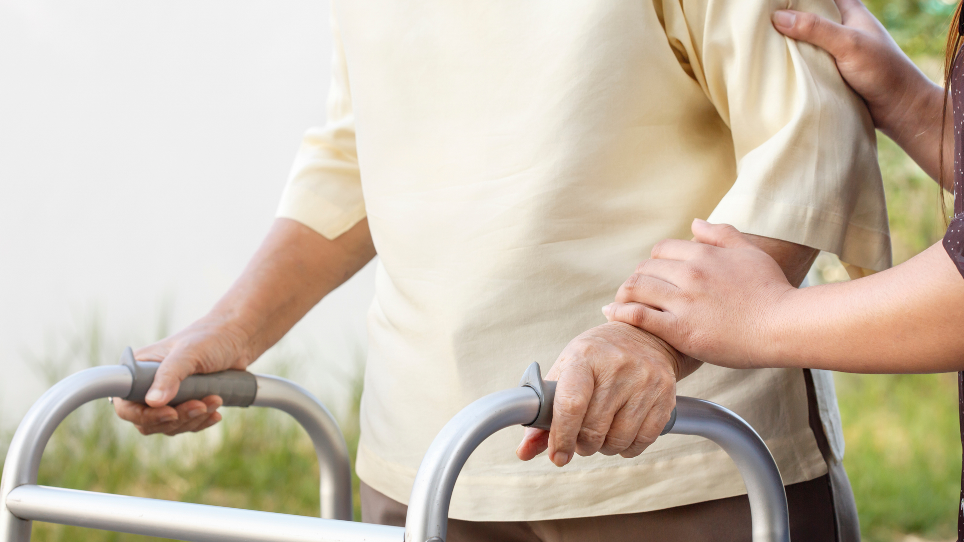Nurse comforts an older woman, hand on her shoulder, both looking up with smiling expressions in a kitchen setting.