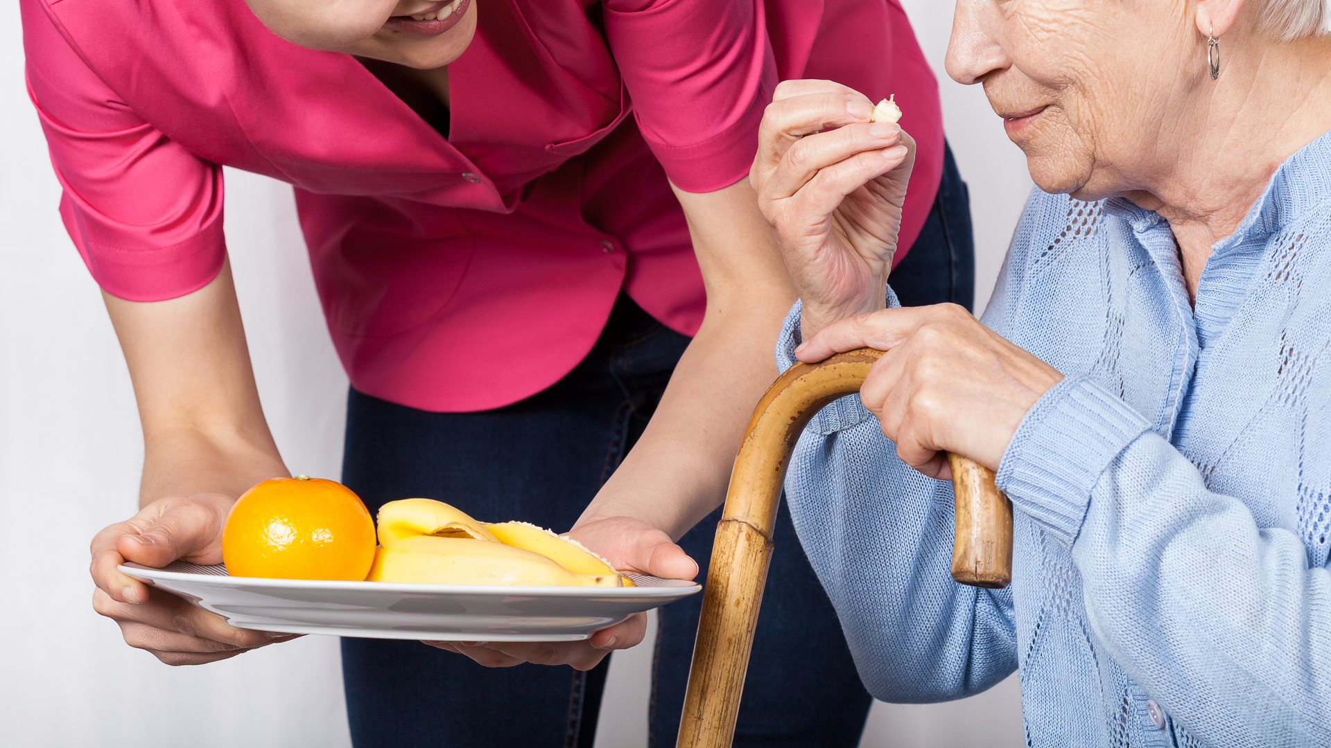 Caregiver showing laptop to senior on a couch, indoors. They both are smiling.