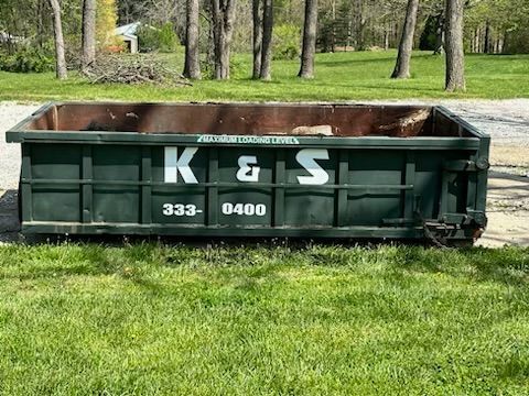 A green dumpster is sitting on top of a lush green field.