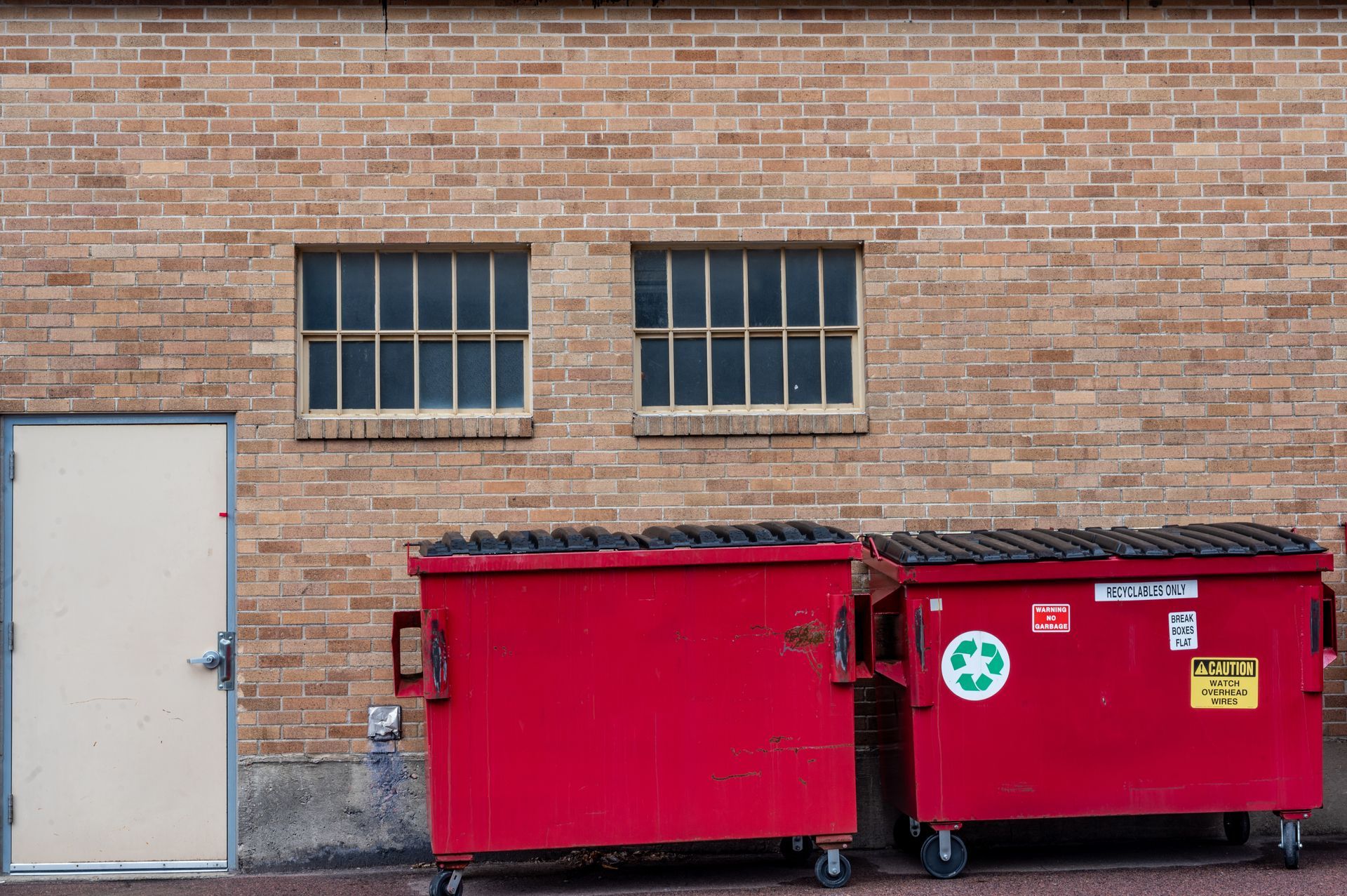 Row of covered garbage bins along a brick wall.