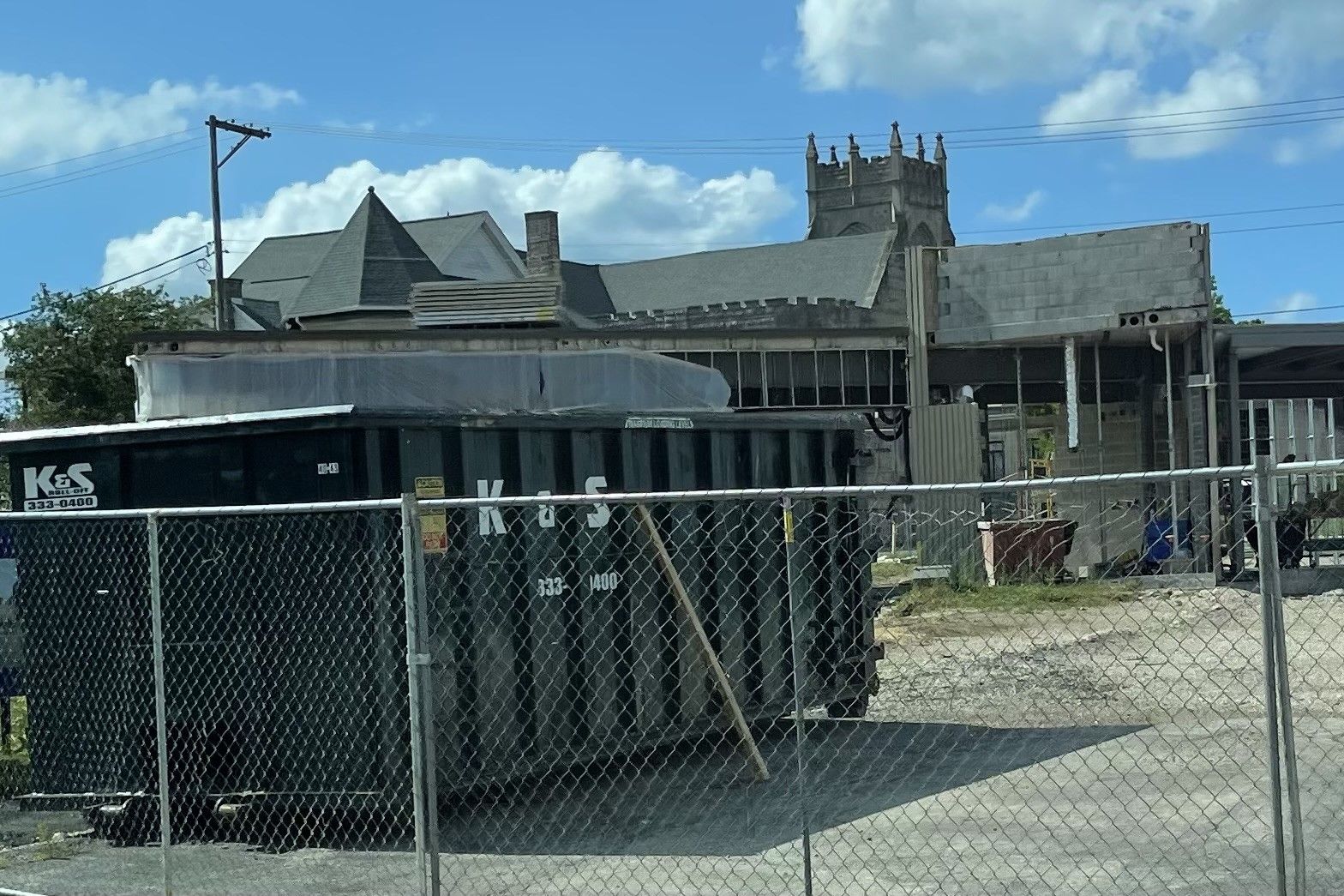 A large black dumpster is behind a chain link fence in front of a building.