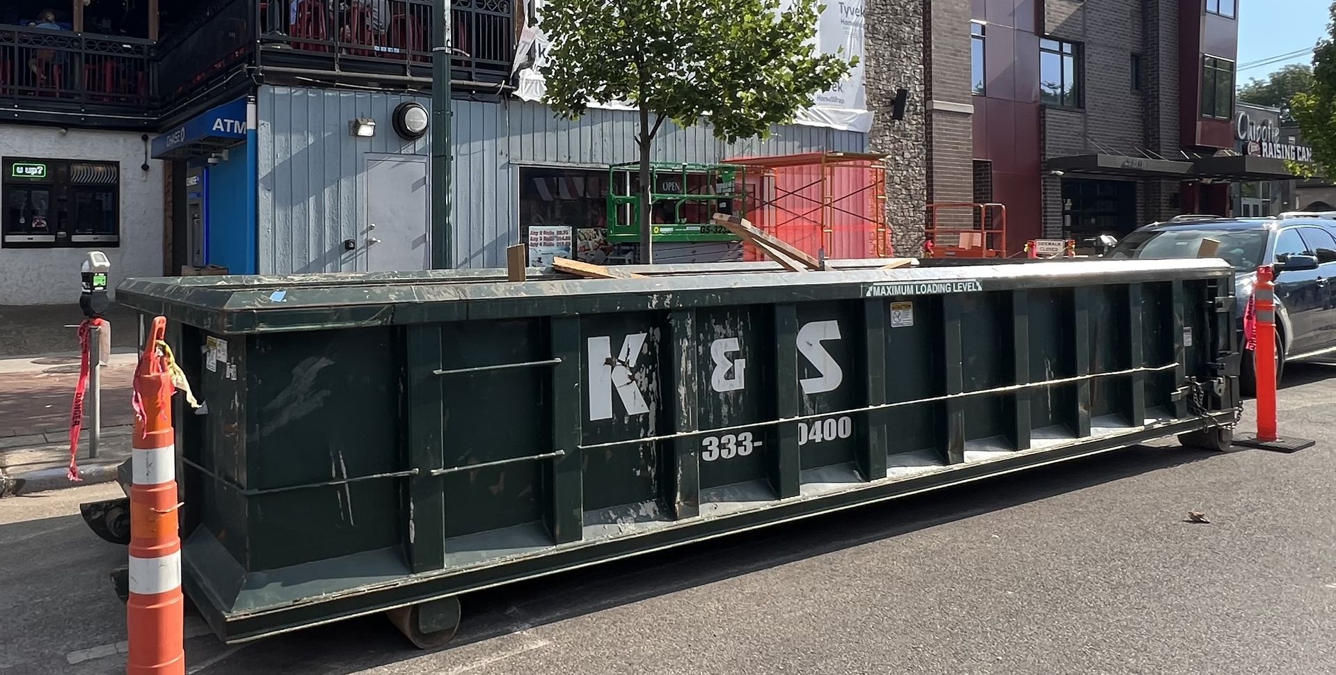 A large dumpster is parked on the side of the road in front of a building.
