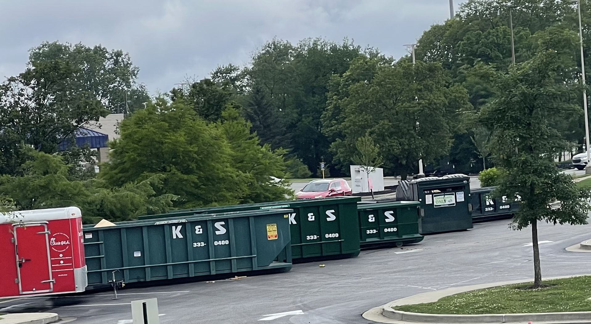 A row of dumpsters are lined up in a parking lot.