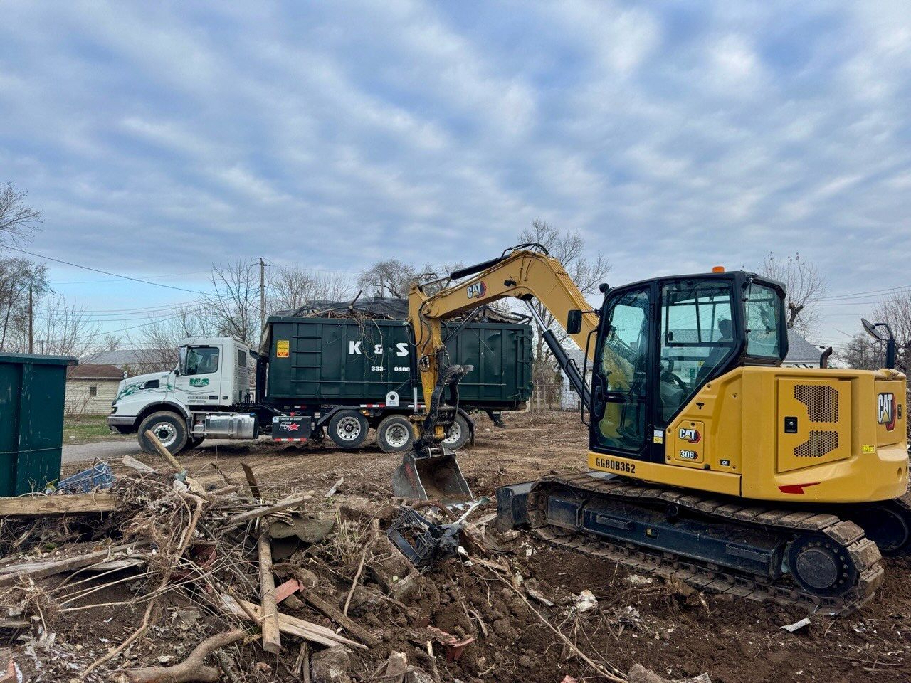 A yellow excavator is loading a dumpster into a truck.