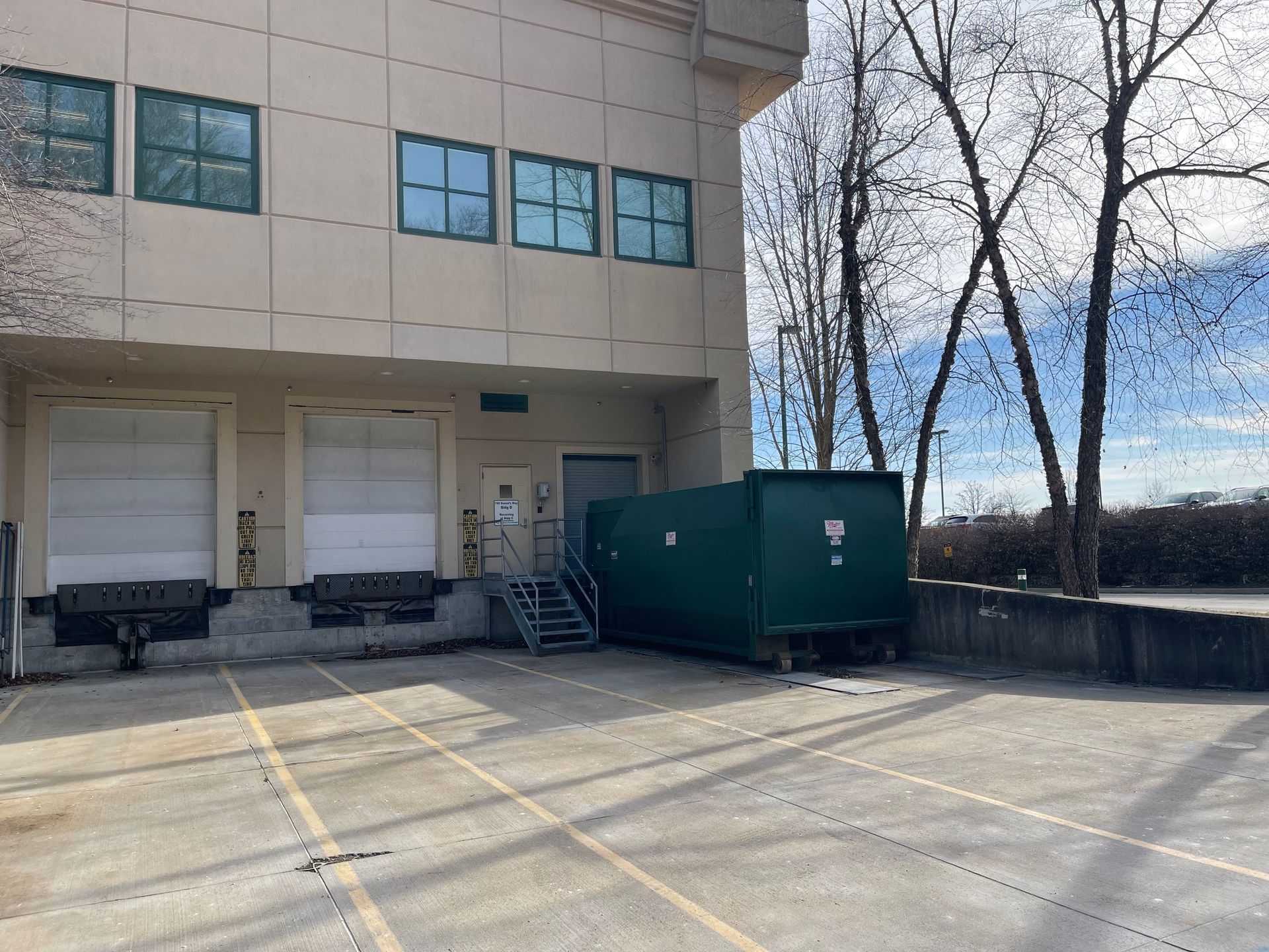 A large green dumpster is parked in front of a large building.