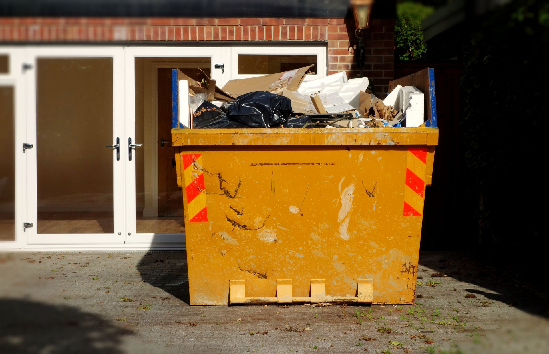 A yellow dumpster full of rubbish from a house clearance.