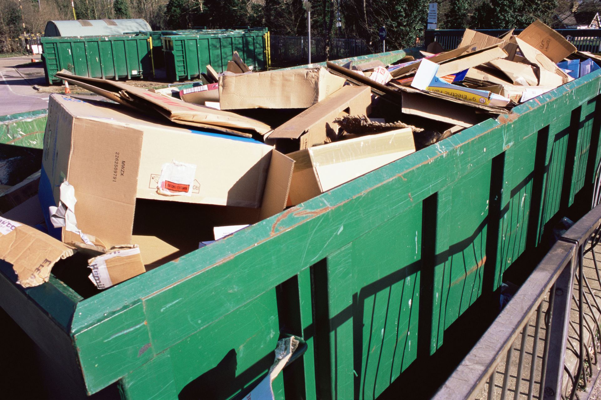 A large green dumpster outdoors full of cardboard boxes.