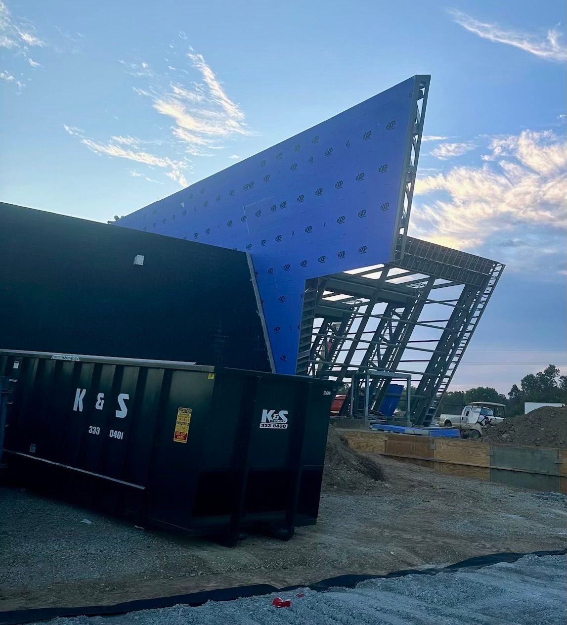 A large black dumpster is parked in front of a building under construction.