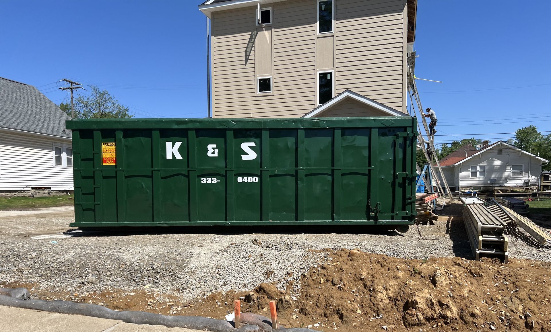 A large green dumpster is parked in front of a house.