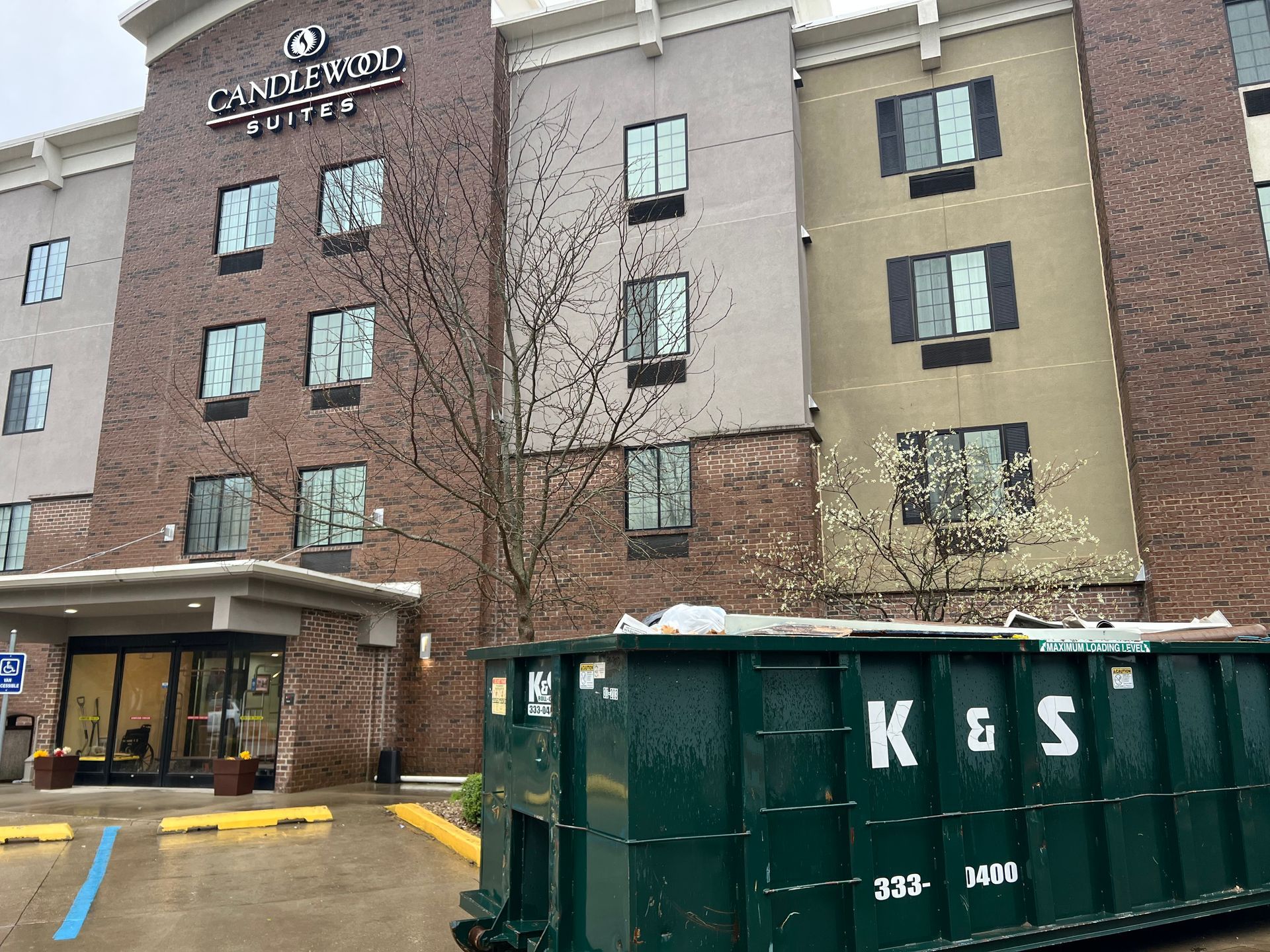 A green dumpster is parked in front of a large brick building.