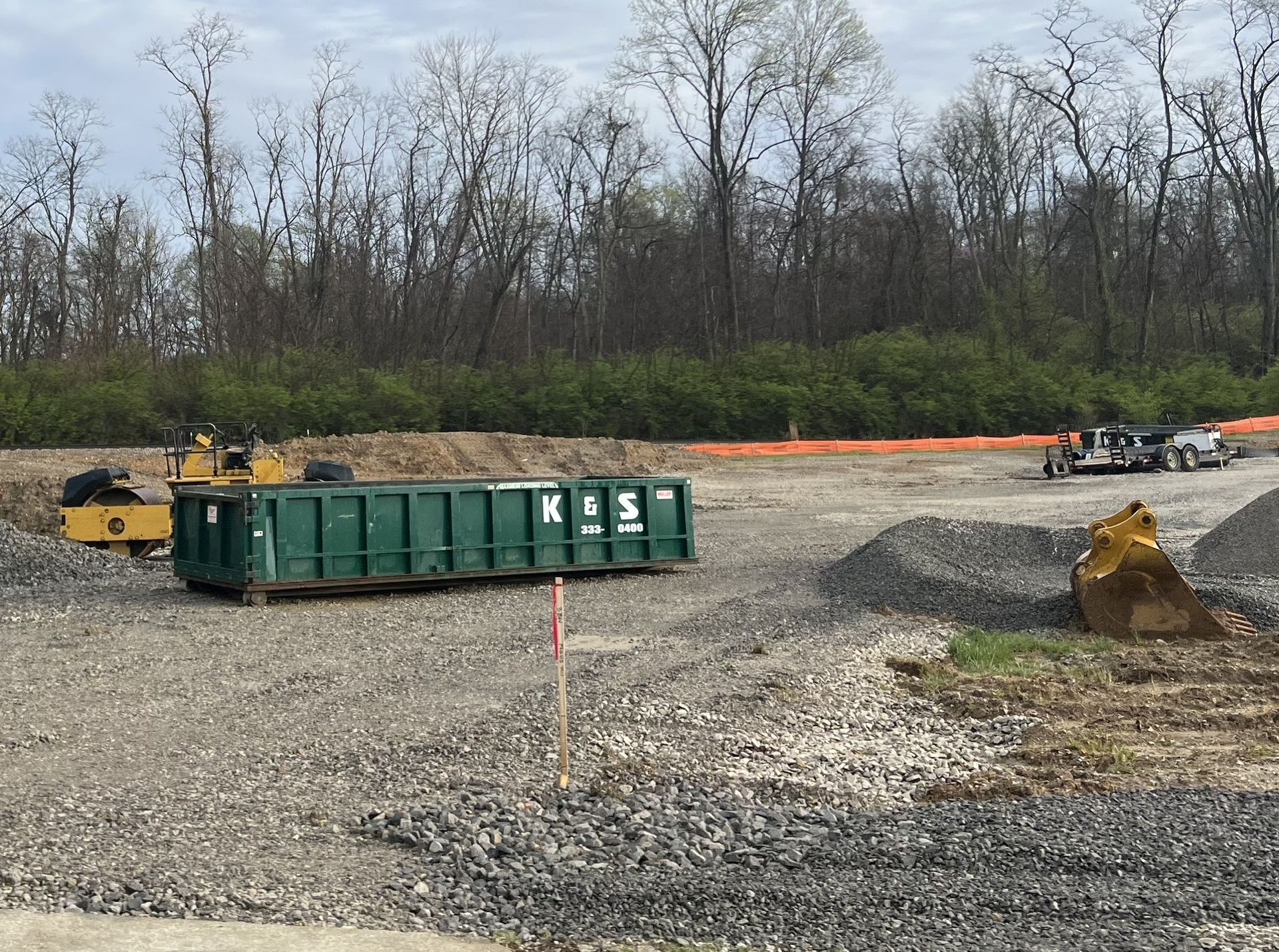 A large green dumpster is sitting in the middle of a dirt field.