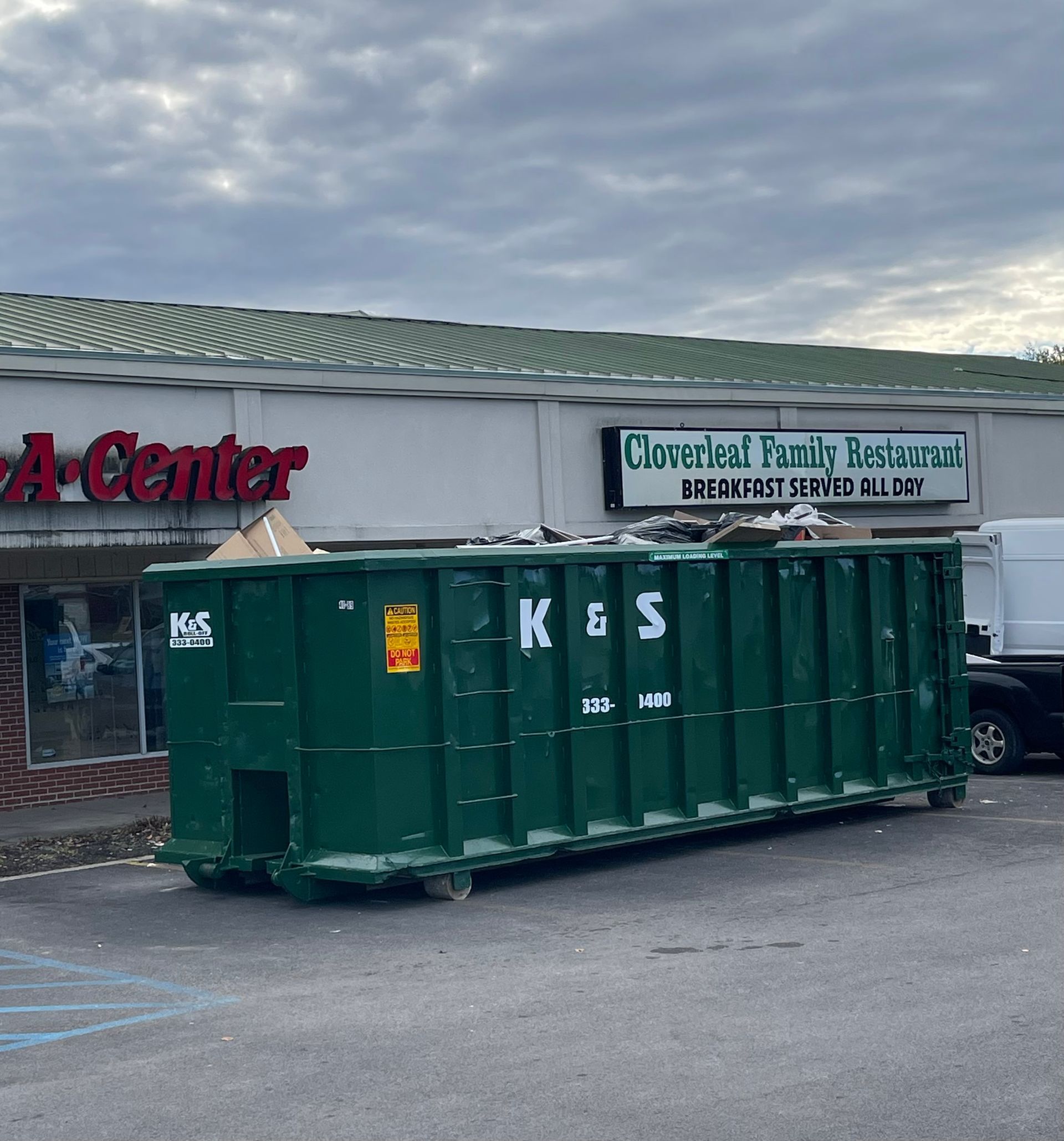 A large green dumpster is parked in front of a store called a center