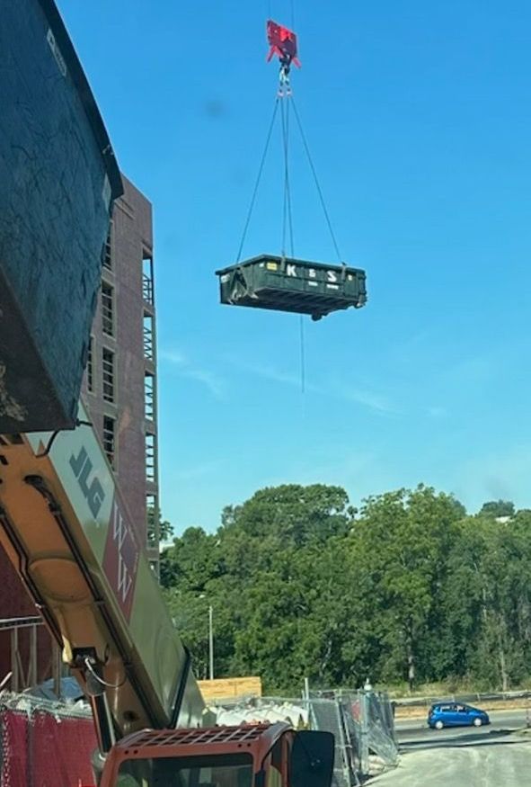 A crane is lifting a dumpster into the air.