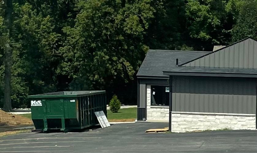 A large green dumpster is parked in front of a store called a center