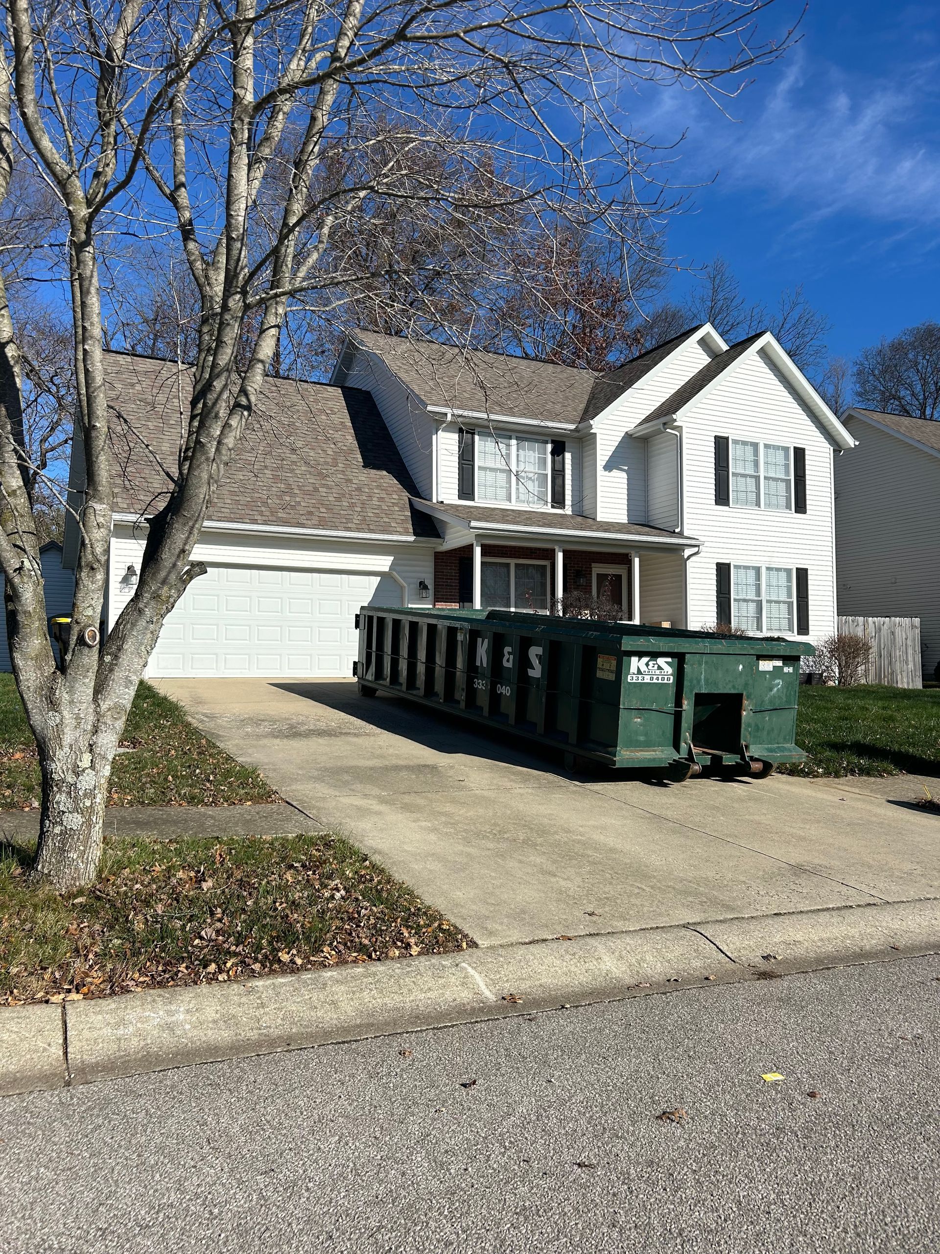 A large white house with a green dumpster in front of it.