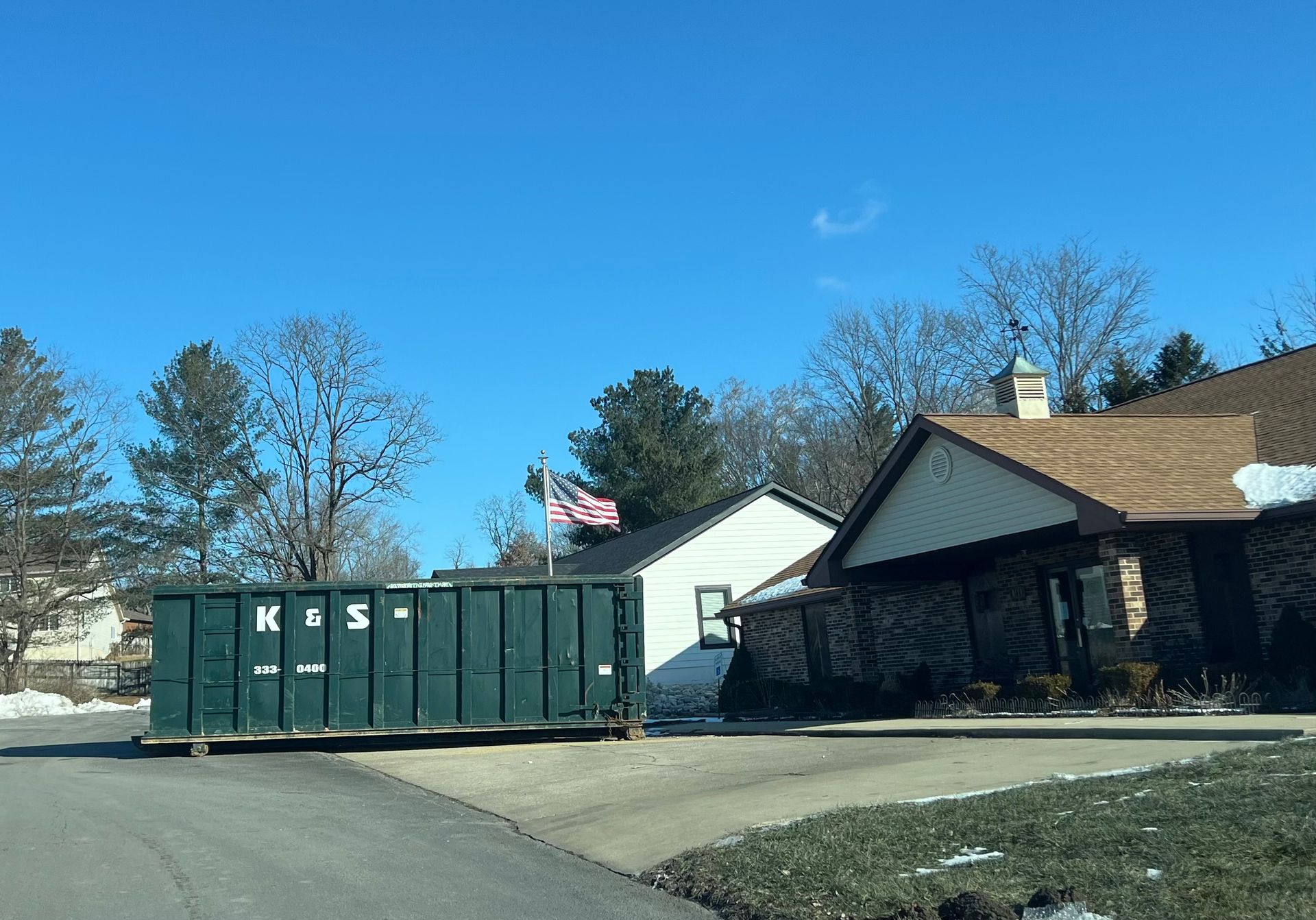 A large green dumpster is parked in front of a house.