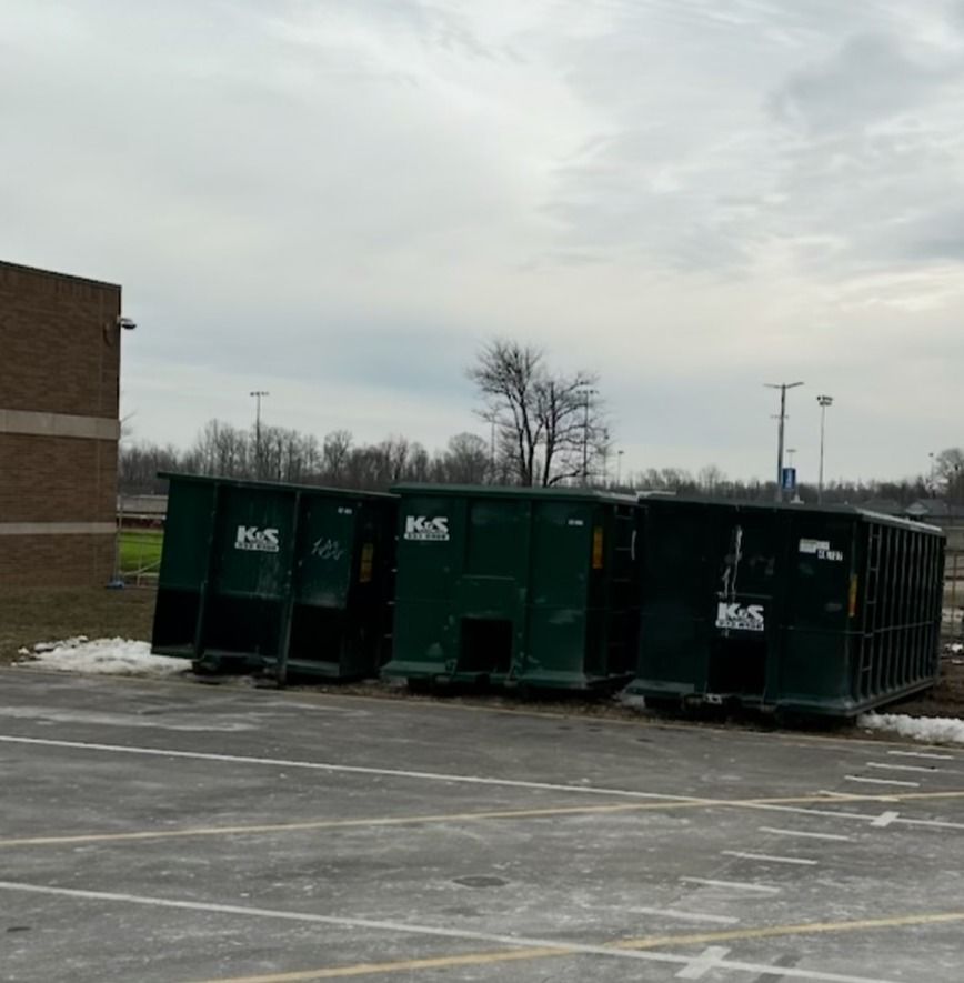 A row of dumpsters are parked in a parking lot