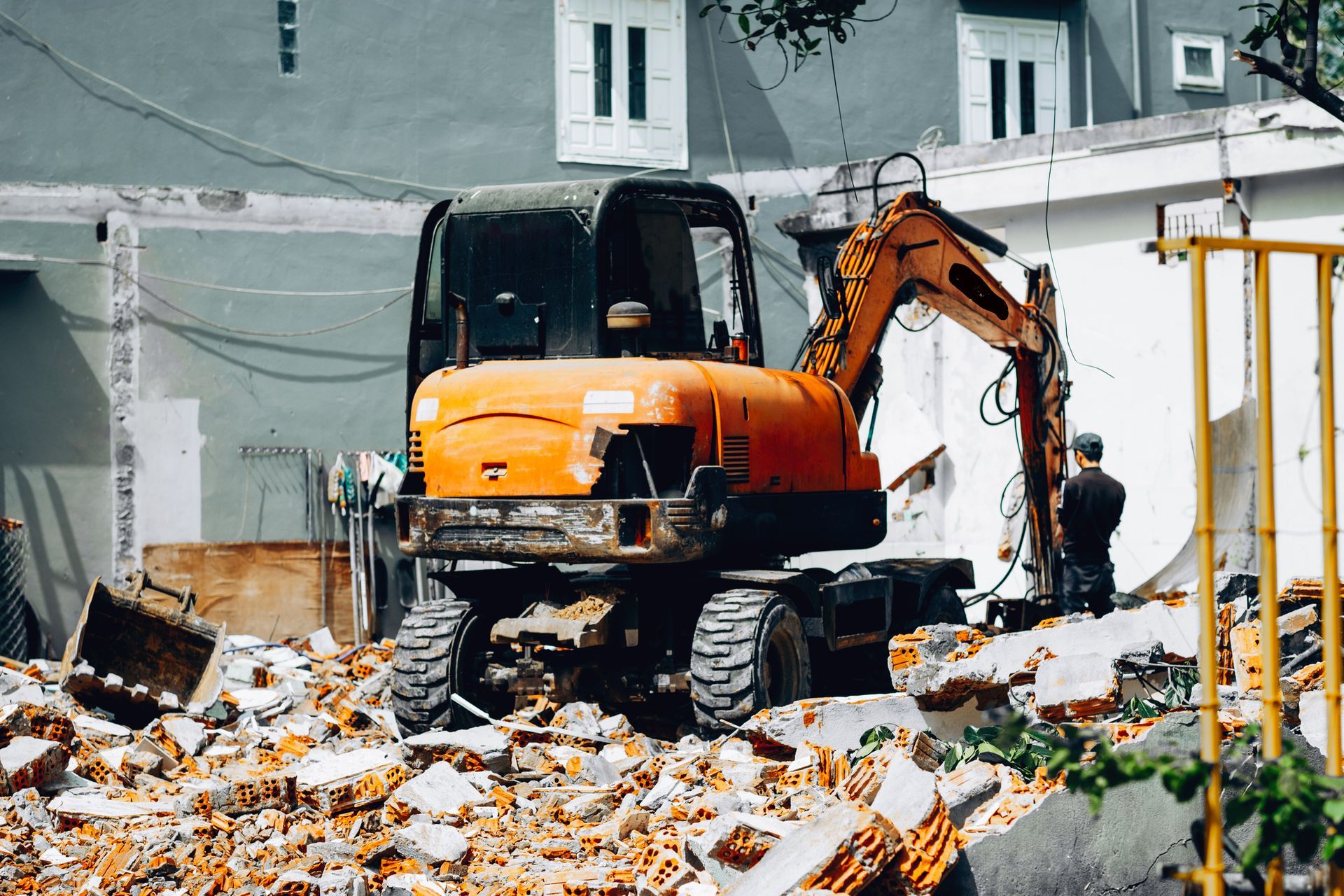 An orange excavator stands among piles of broken bricks and debris in a construction site.
