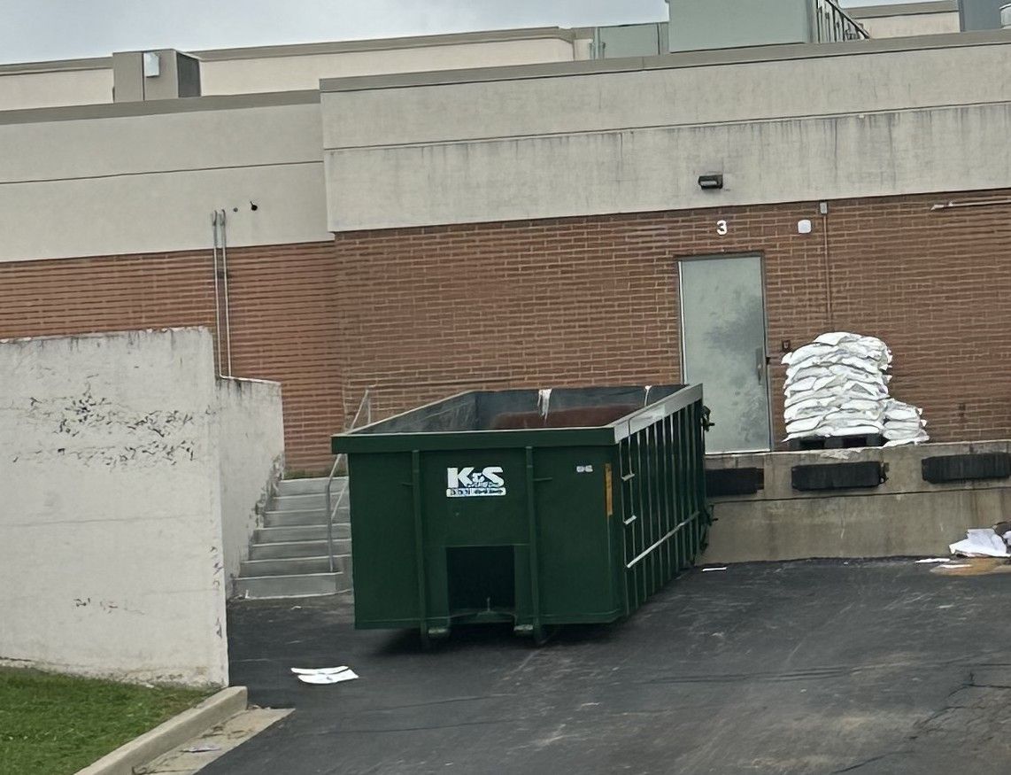 A large green dumpster is parked in front of a store called a center